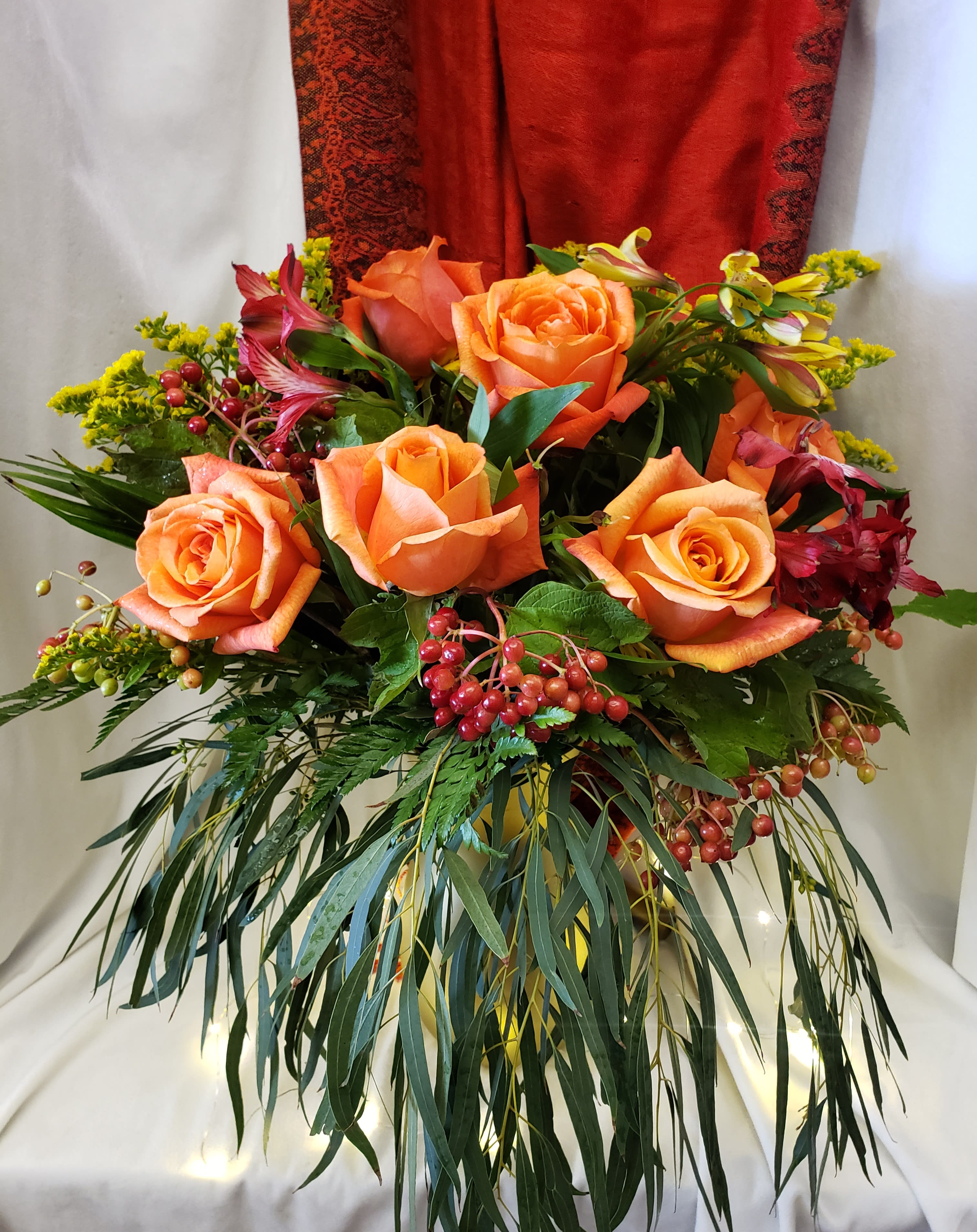 Orange roses arranged with red berries and greenery in a vase