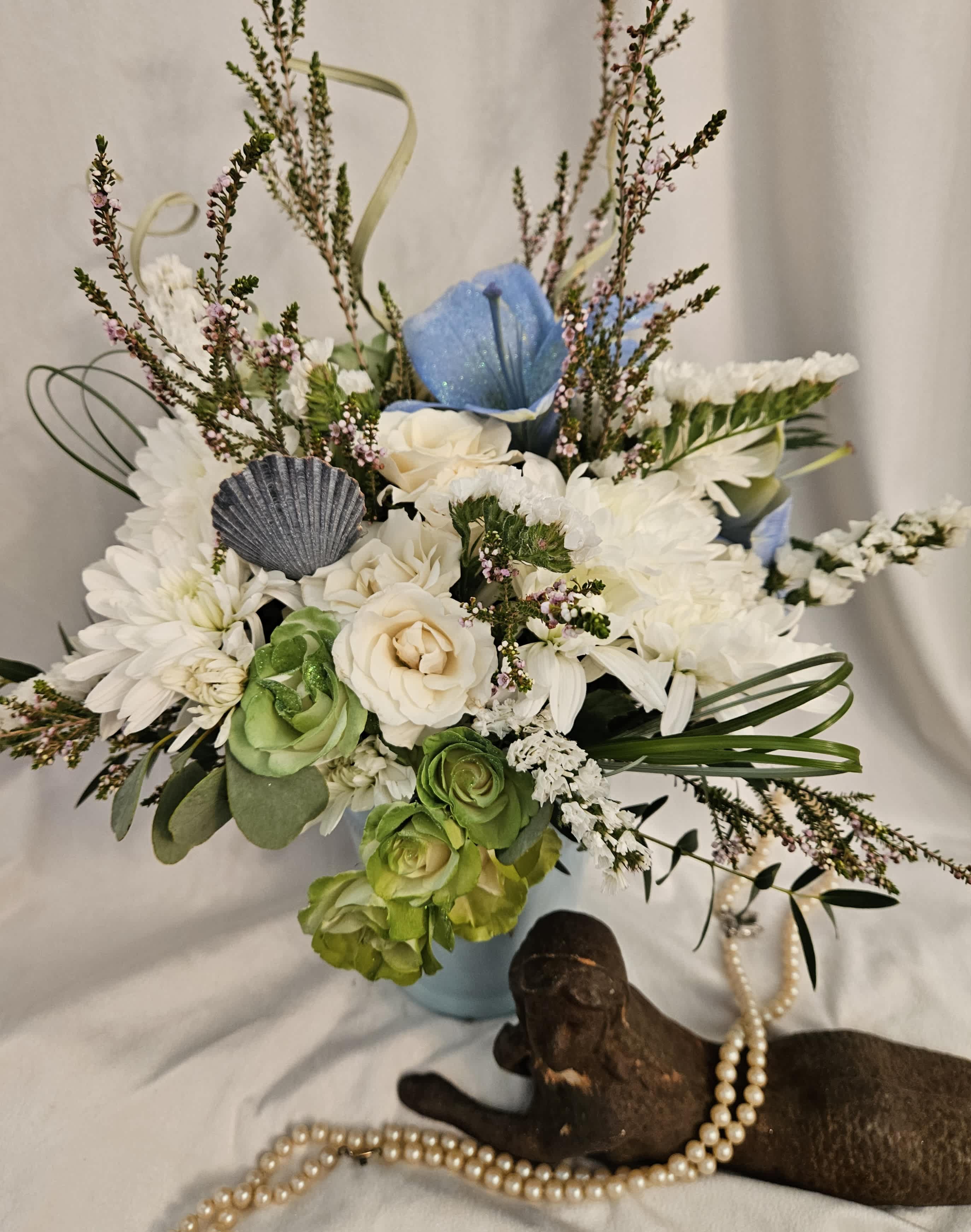 White and blue floral arrangement in a light blue vase with a shell accent