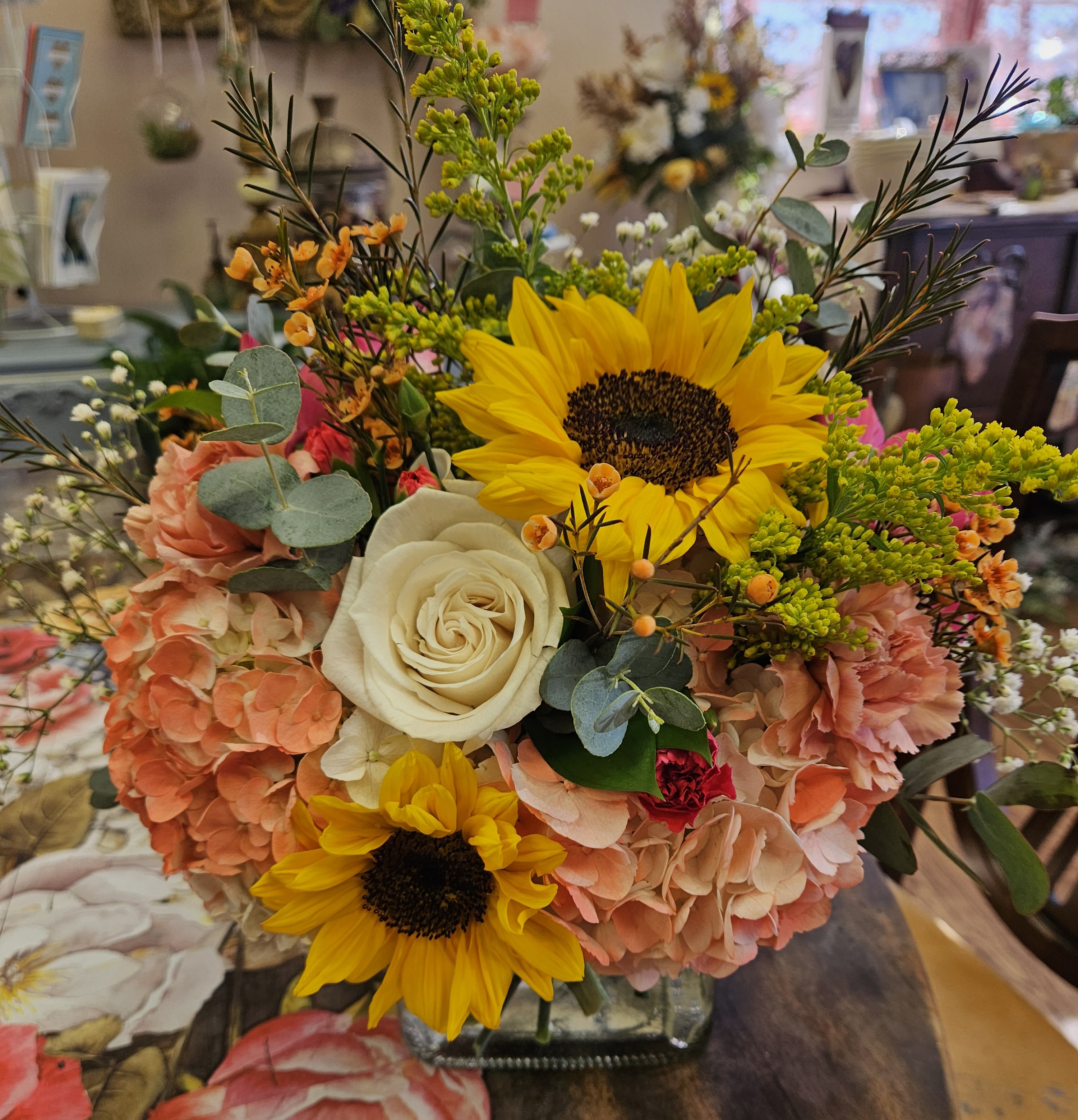 Bouquet with sunflowers, white roses, and peach hydrangeas in a glass vase