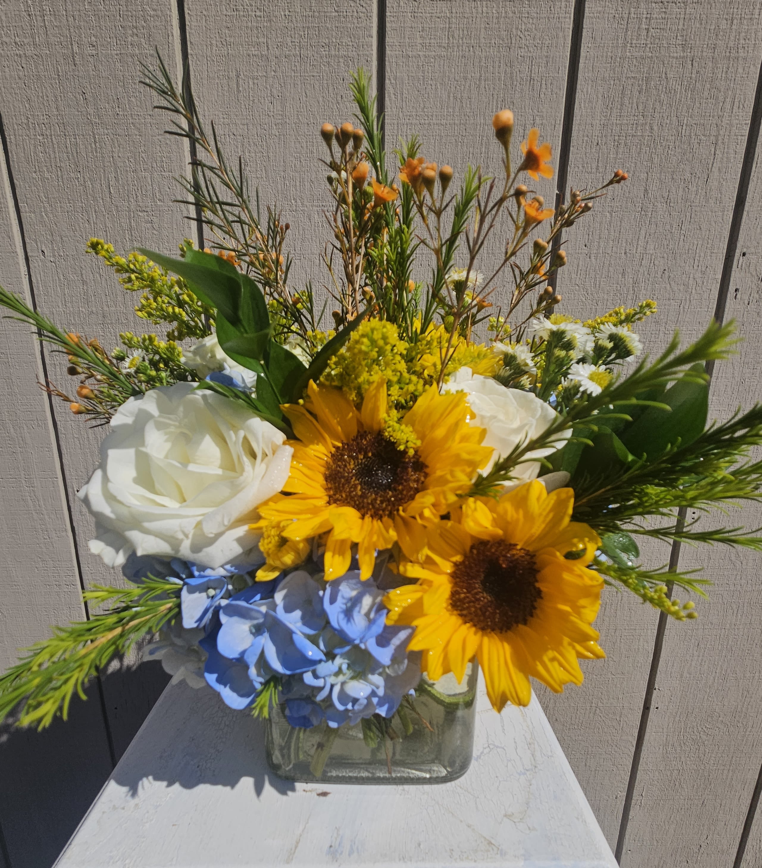 Bouquet of sunflowers, white roses, and blue hydrangea in a glass vase