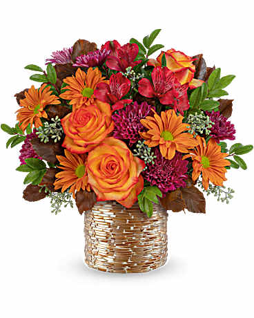 Bouquet of orange roses and mixed autumn flowers in a woven basket vase