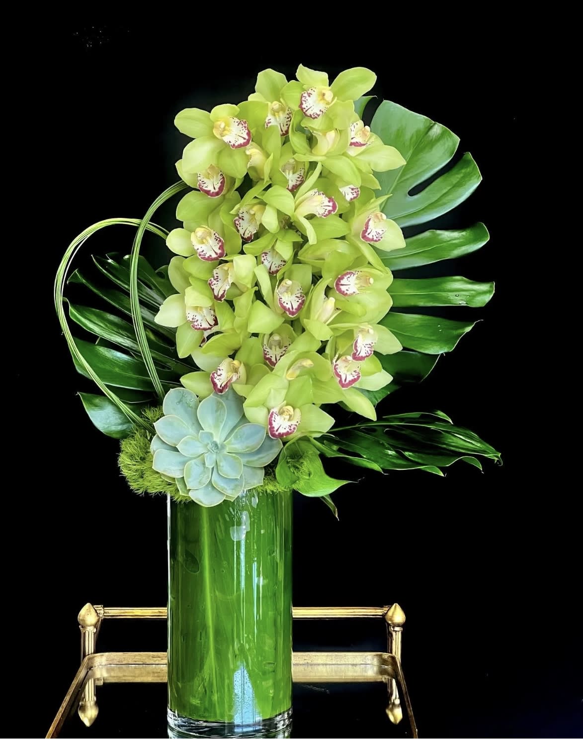 Green orchid arrangement in a tall glass vase with a succulent accent