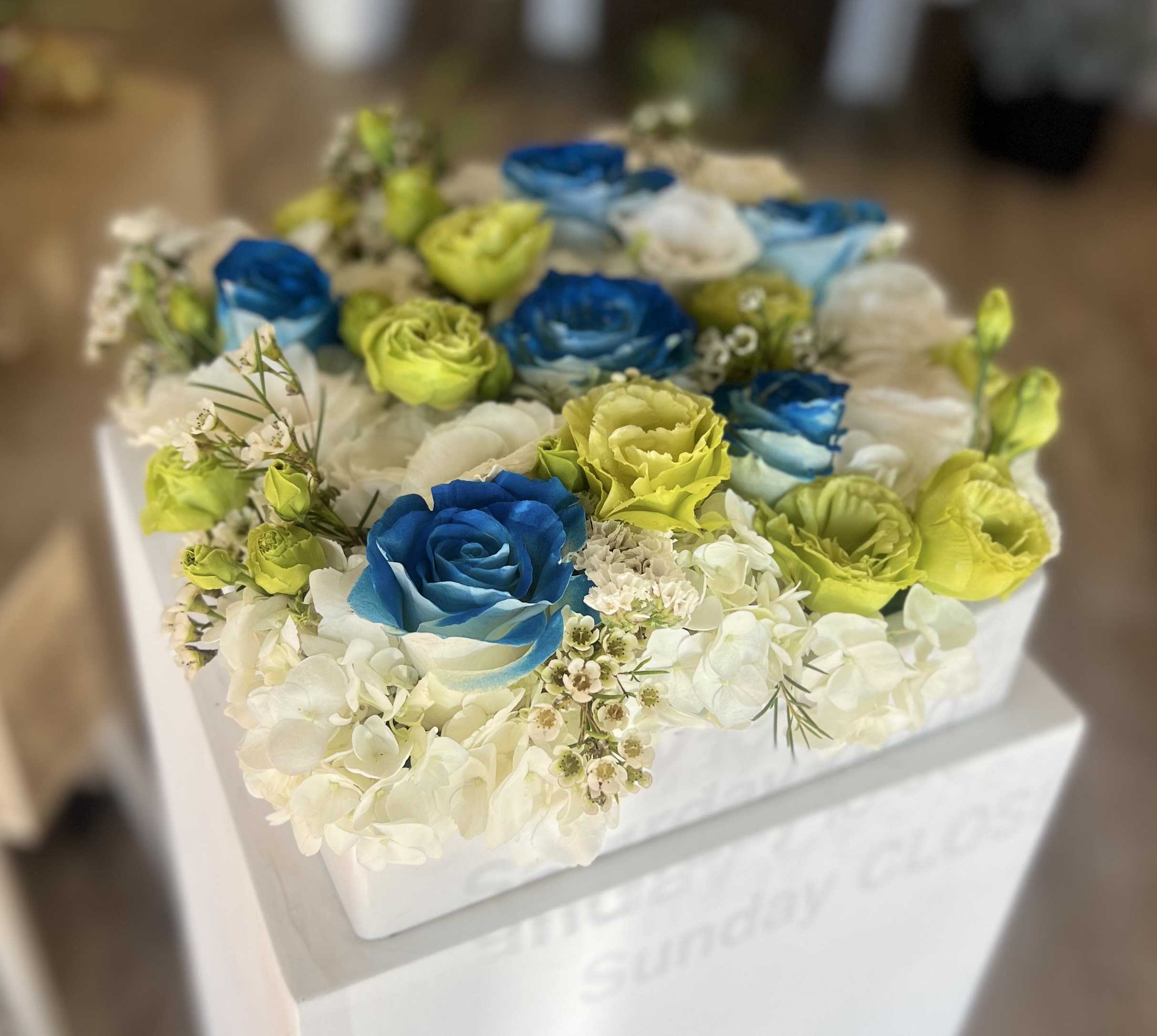 Box arrangement of blue and lime roses with white hydrangeas