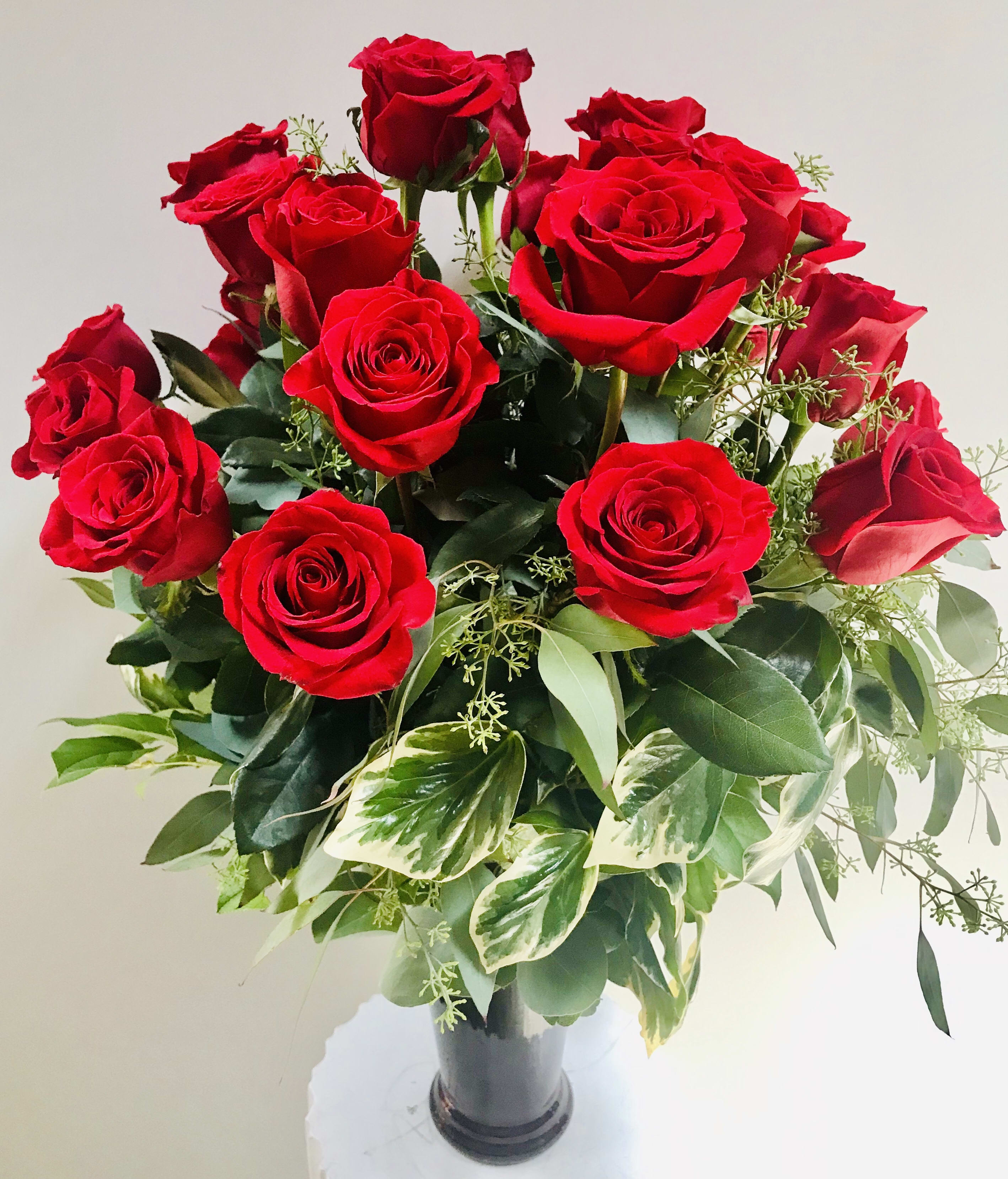 Arrangement of red roses with variegated foliage in a tall dark glass vase