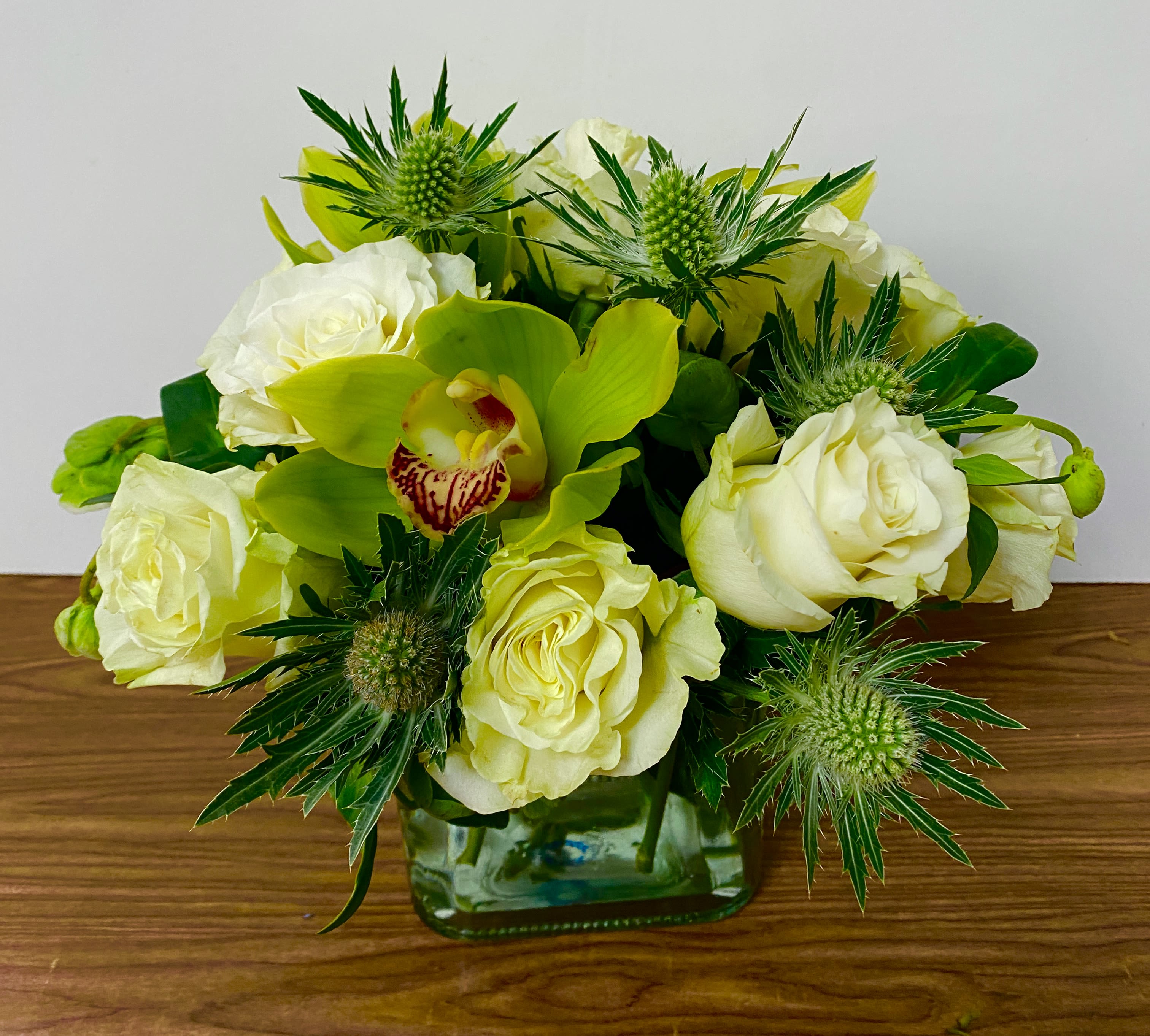 White roses and a green orchid arranged in a square glass vase
