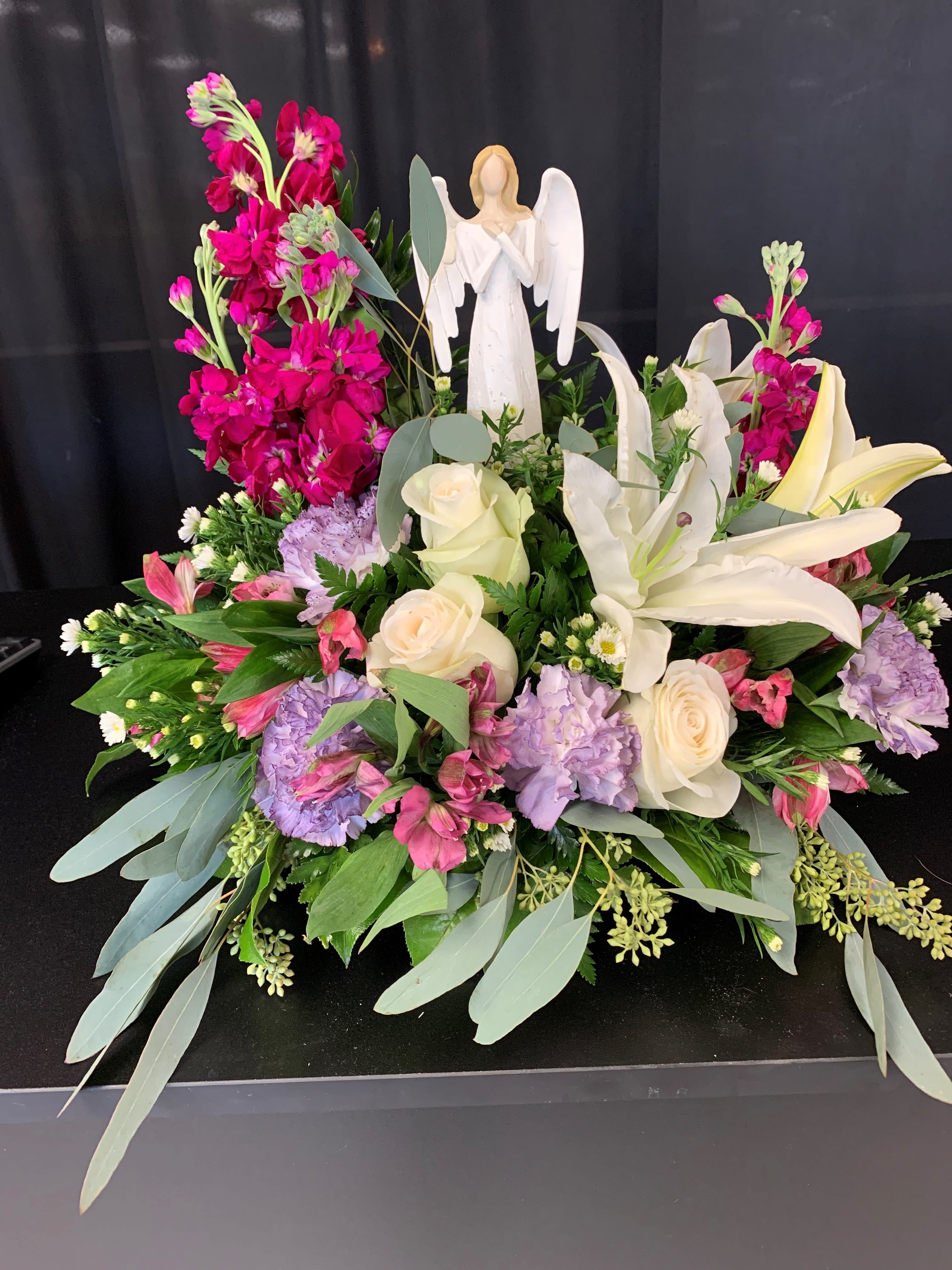 Large floral arrangement with white lilies, roses, and pink blooms around an angel figurine