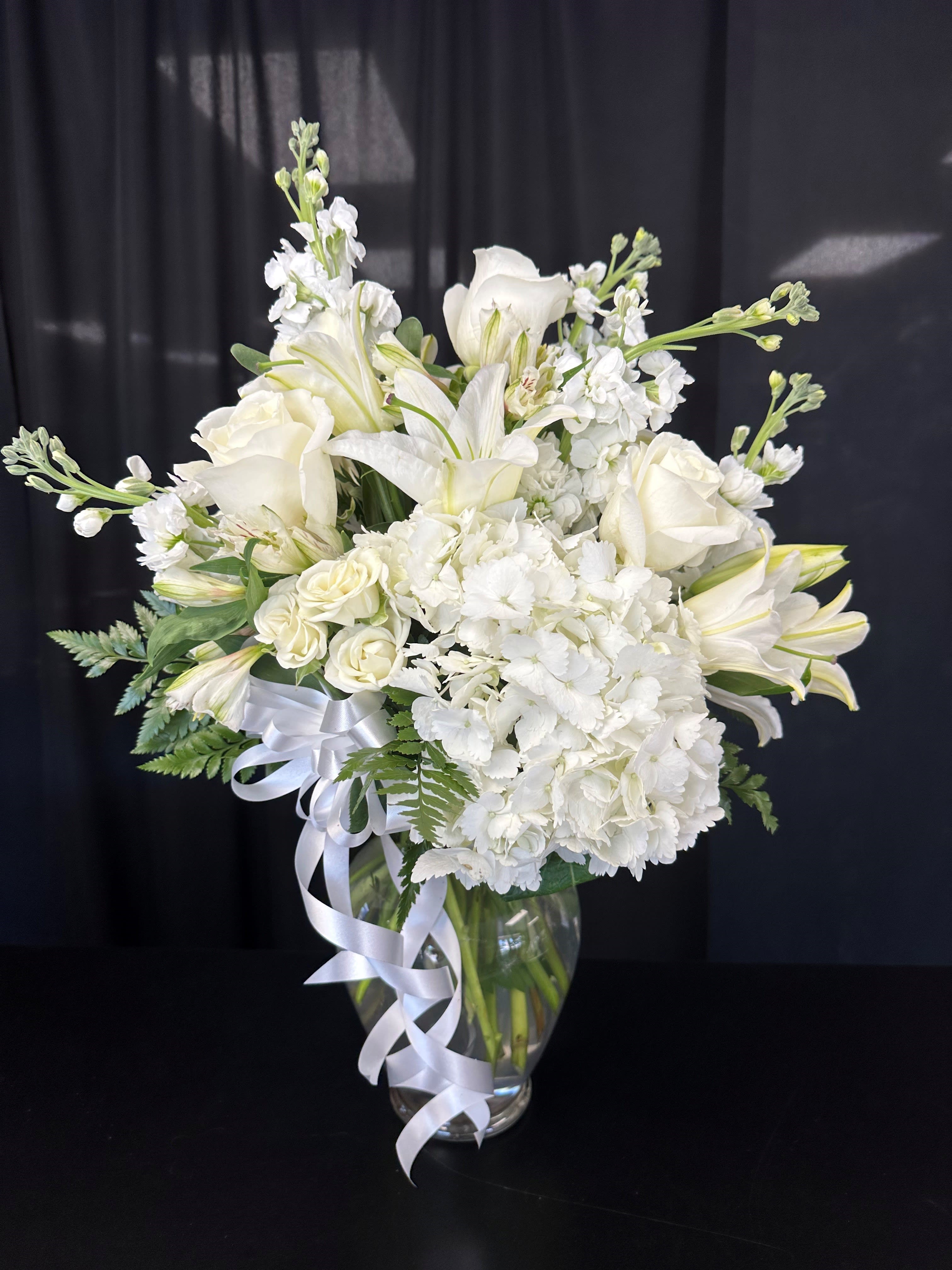 White floral arrangement in a clear glass vase with a white ribbon