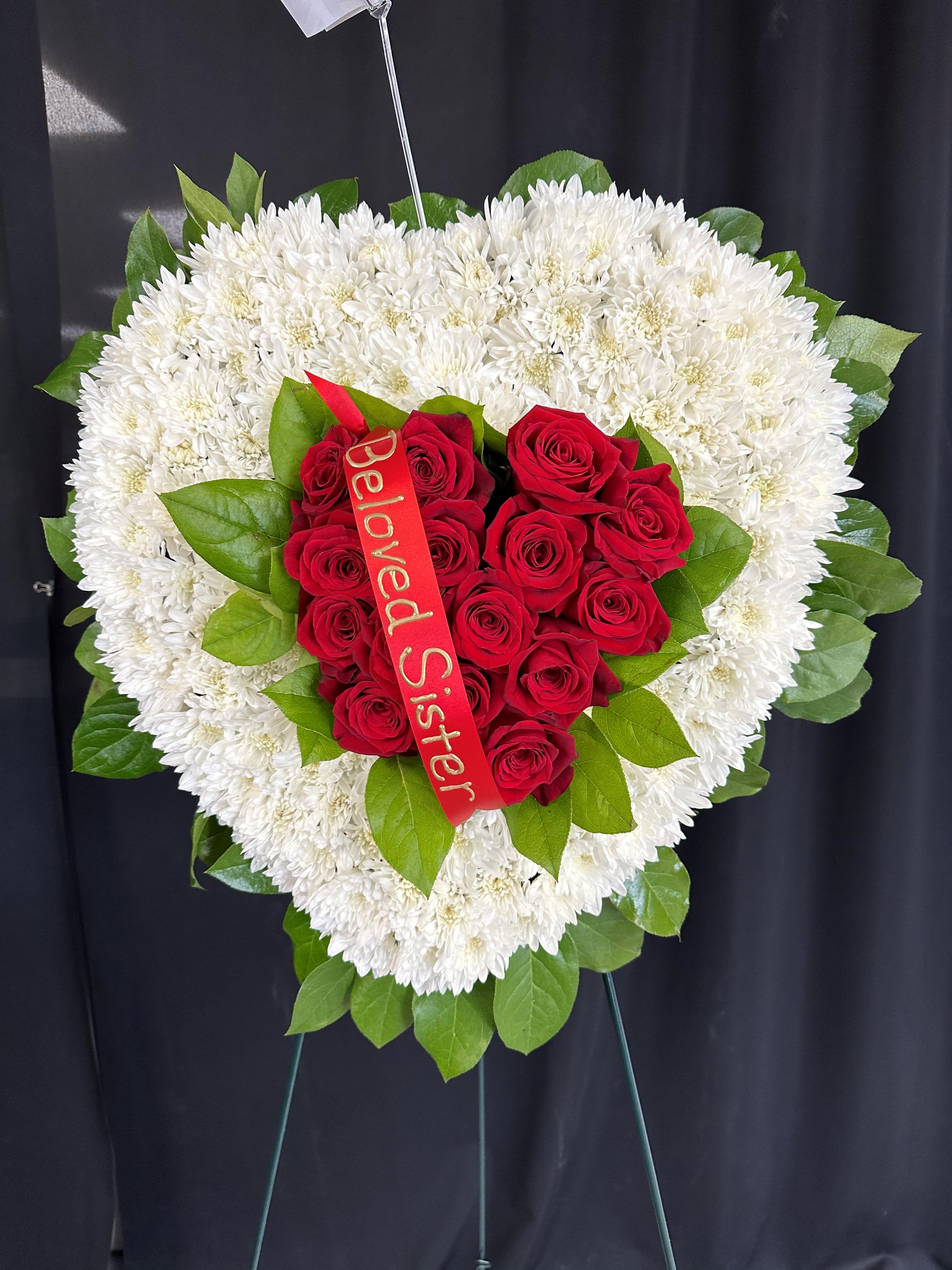 Heart-shaped white chrysanthemum wreath with red roses and a ribbon