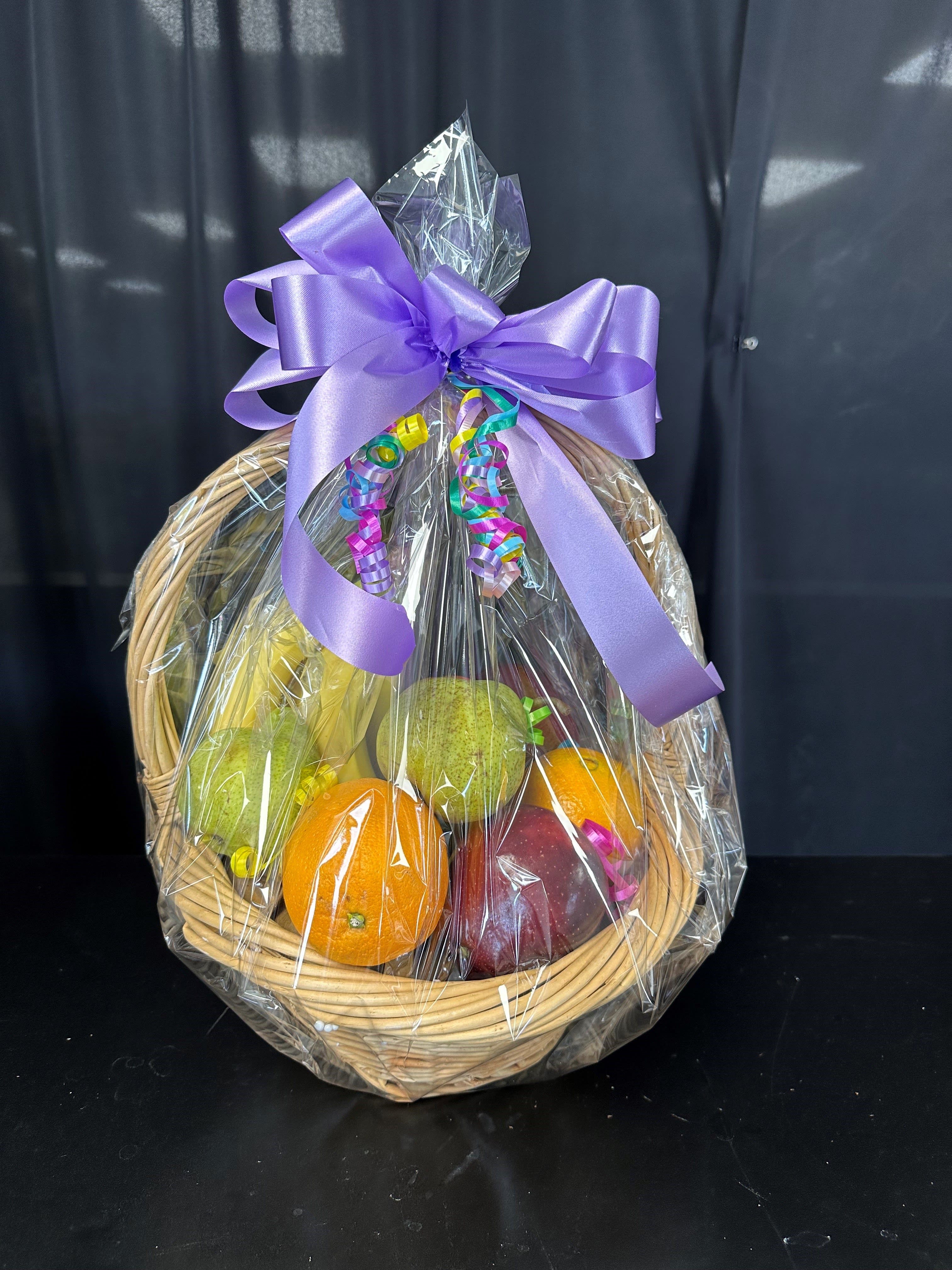 Fruit basket with oranges, pears, and an apple wrapped in clear cellophane