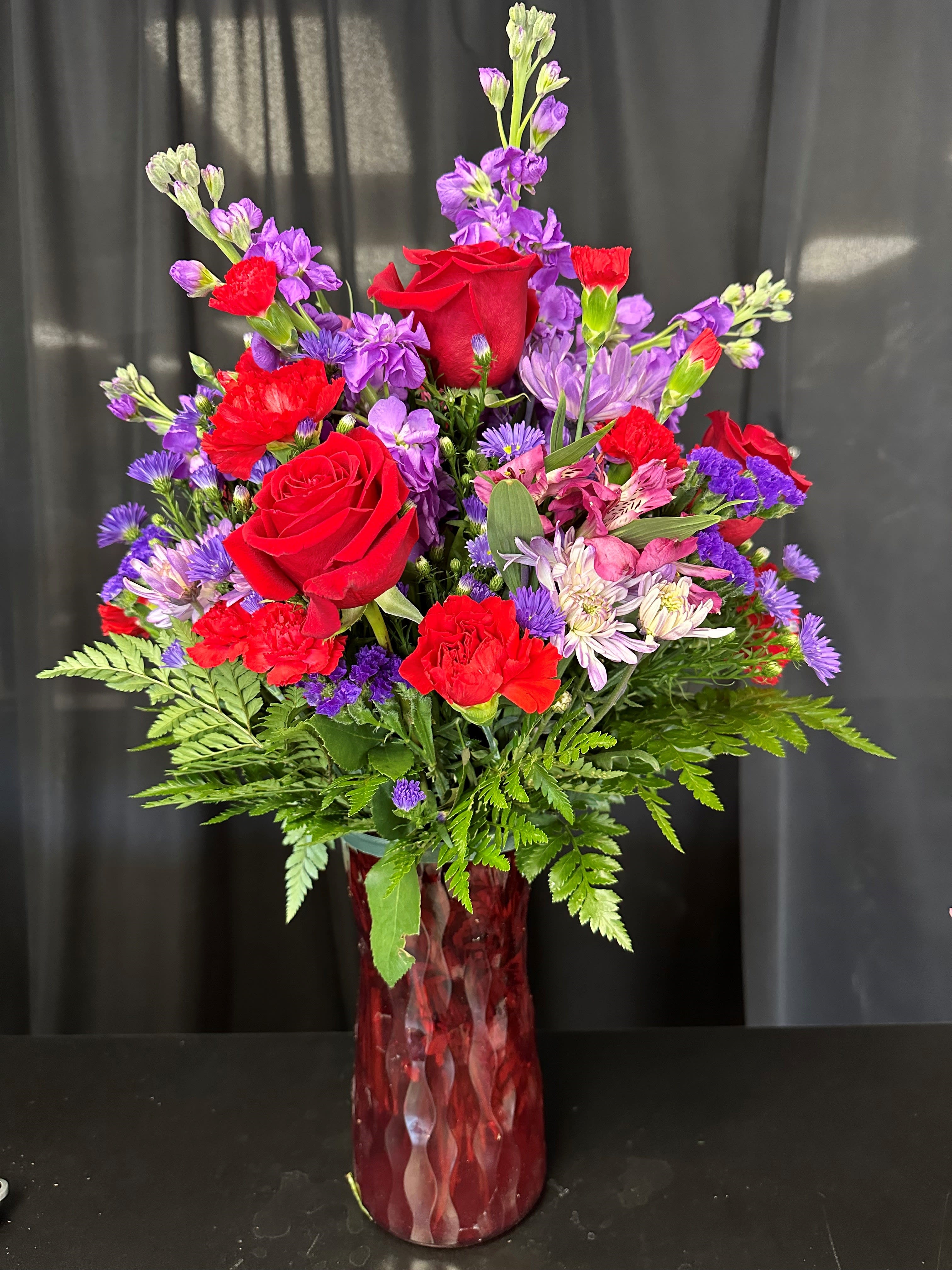 Red roses and purple mixed flowers in a red glass vase