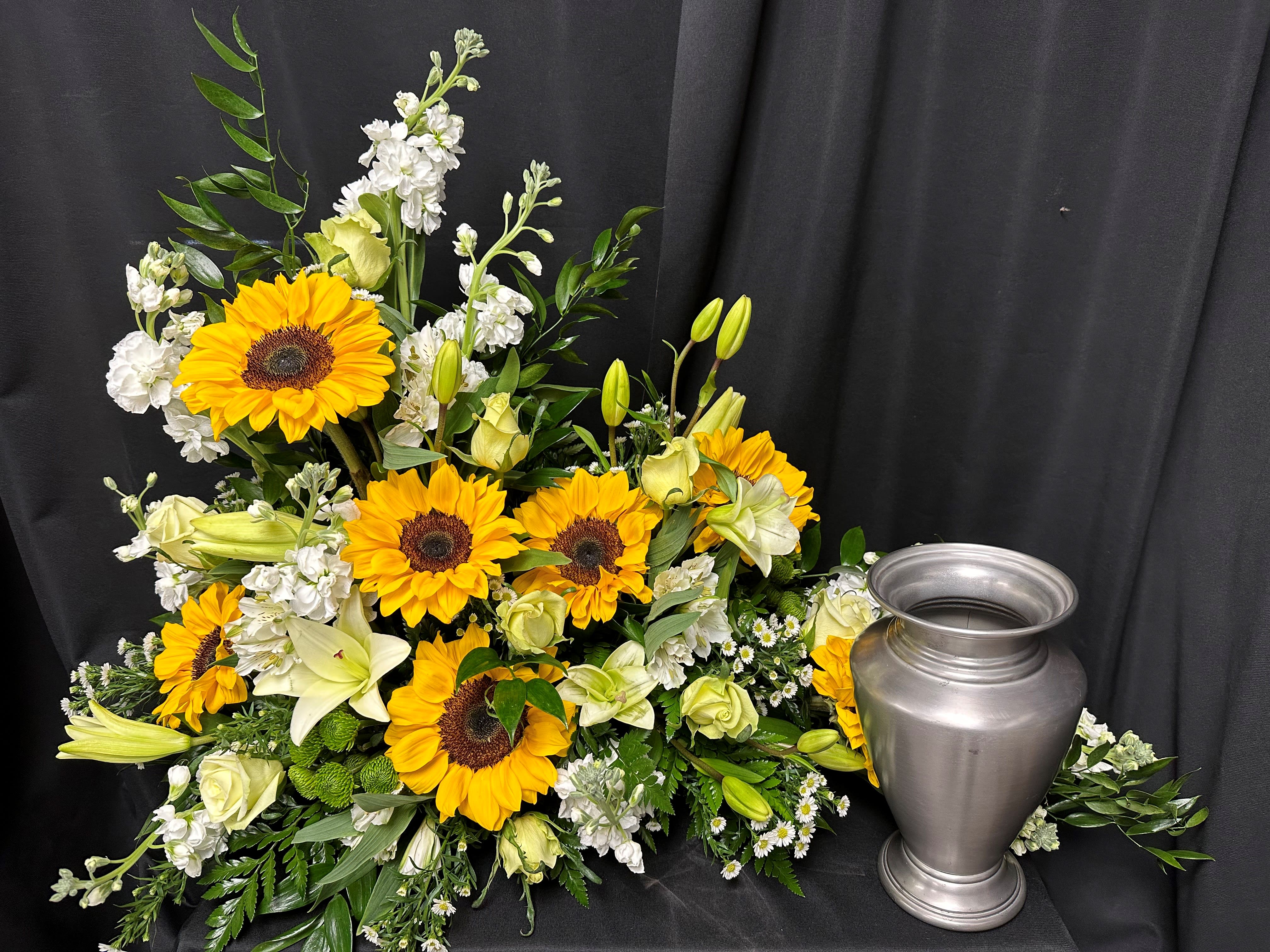 Sunflower and white floral arrangement beside a silver urn