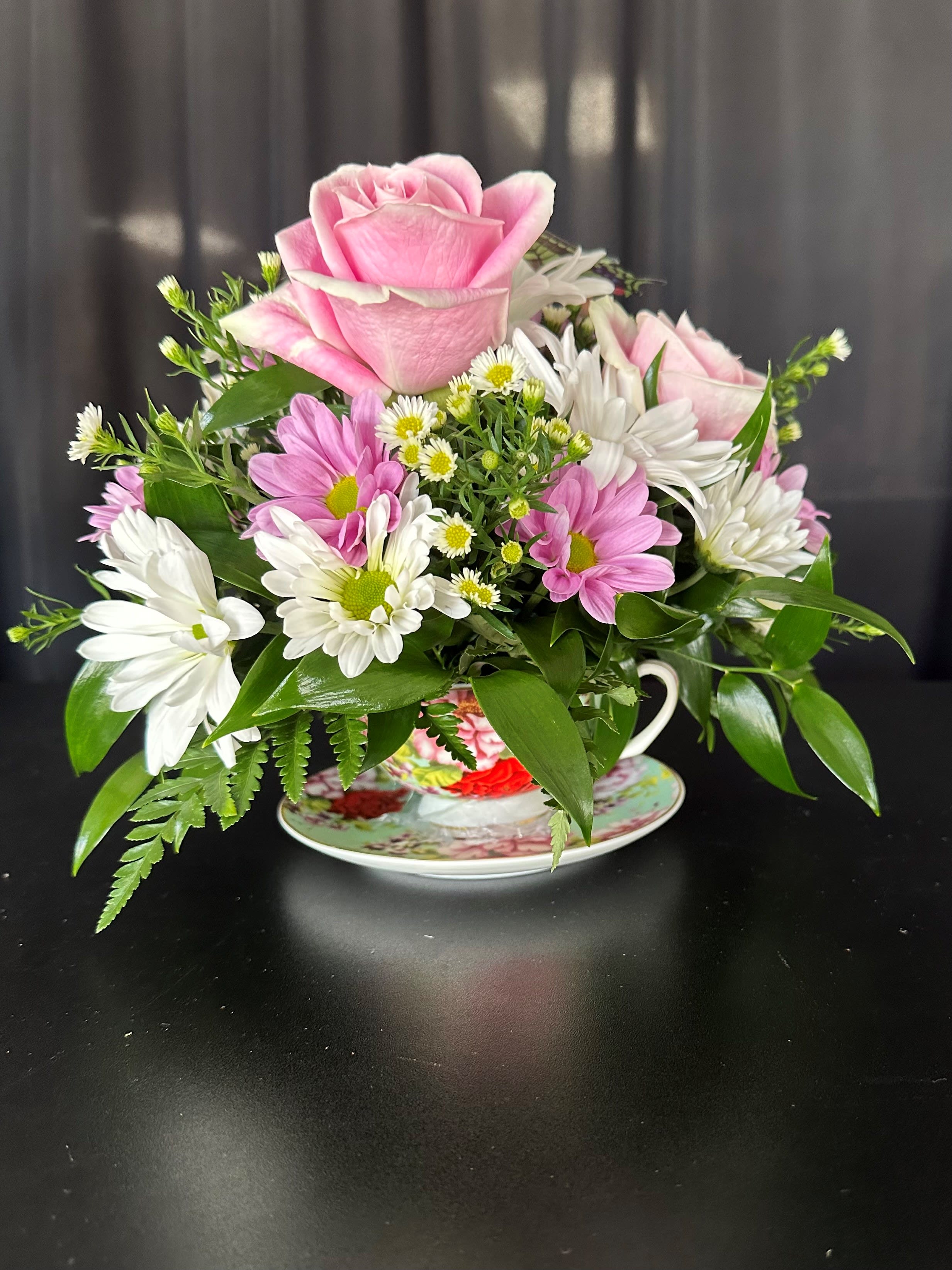 Pink rose and white daisy bouquet in a teacup on a saucer