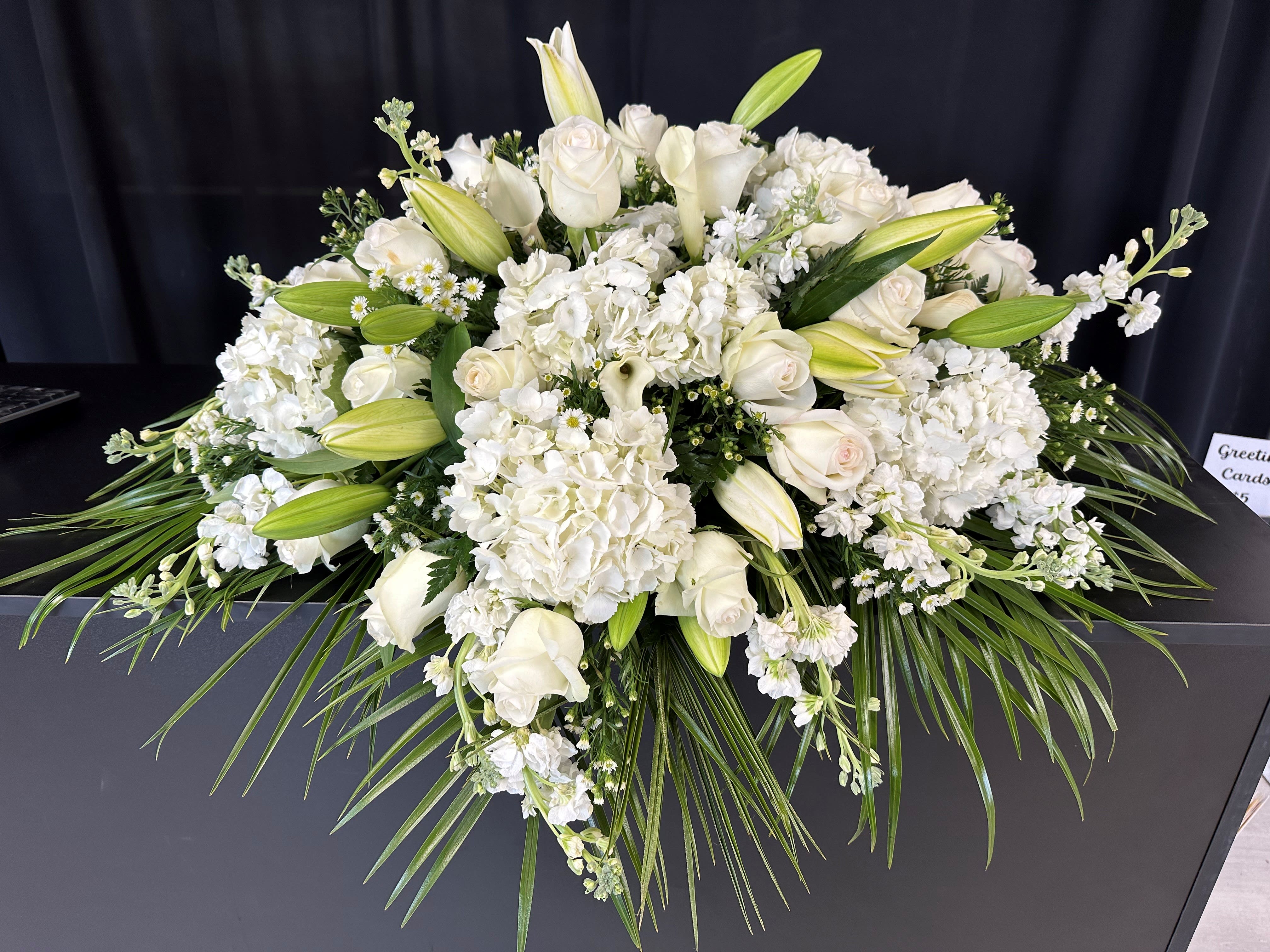 White floral casket spray with roses, lilies, and hydrangeas