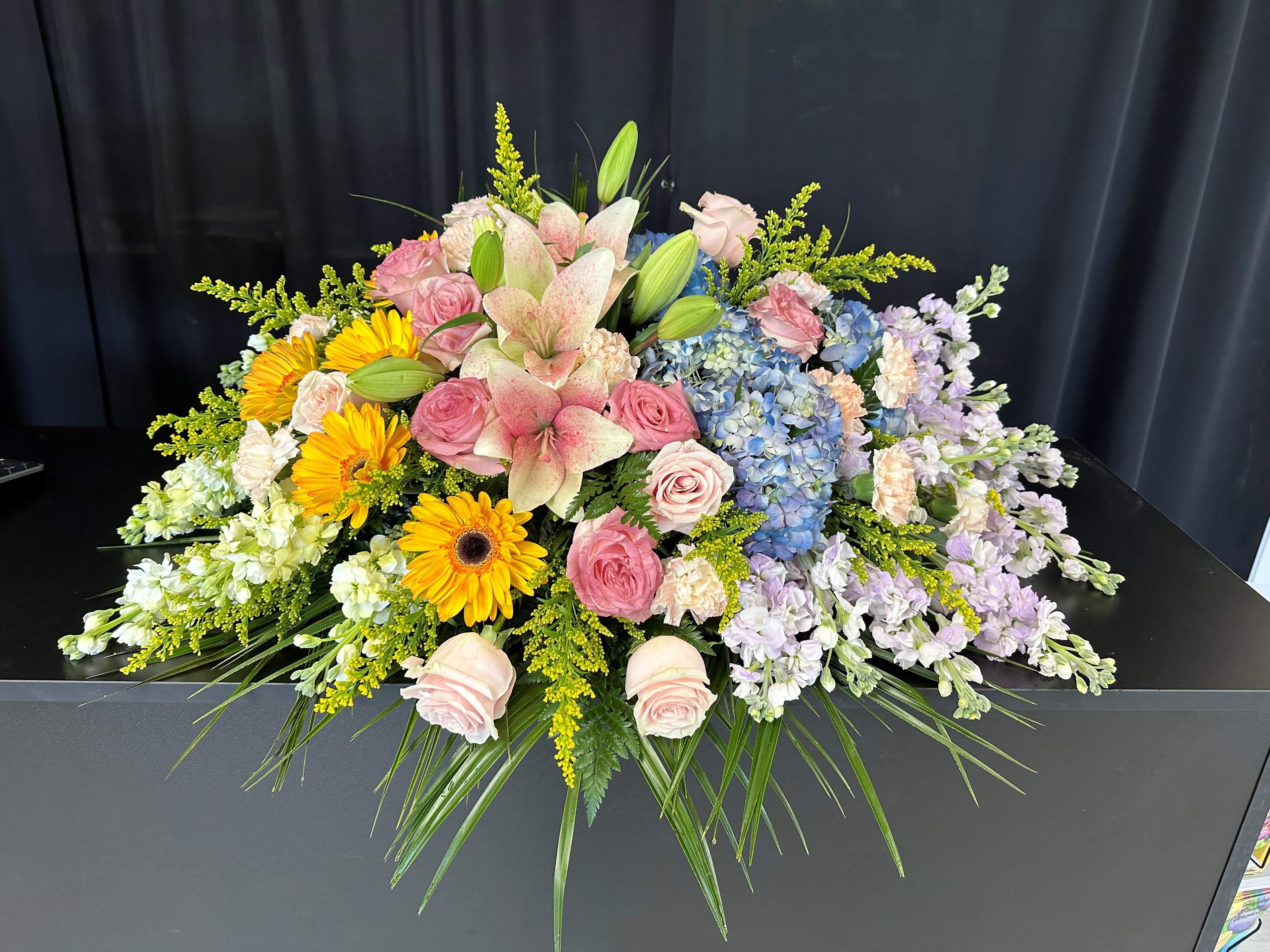 Large floral casket spray with pink roses, lilies, hydrangeas, and yellow daisies