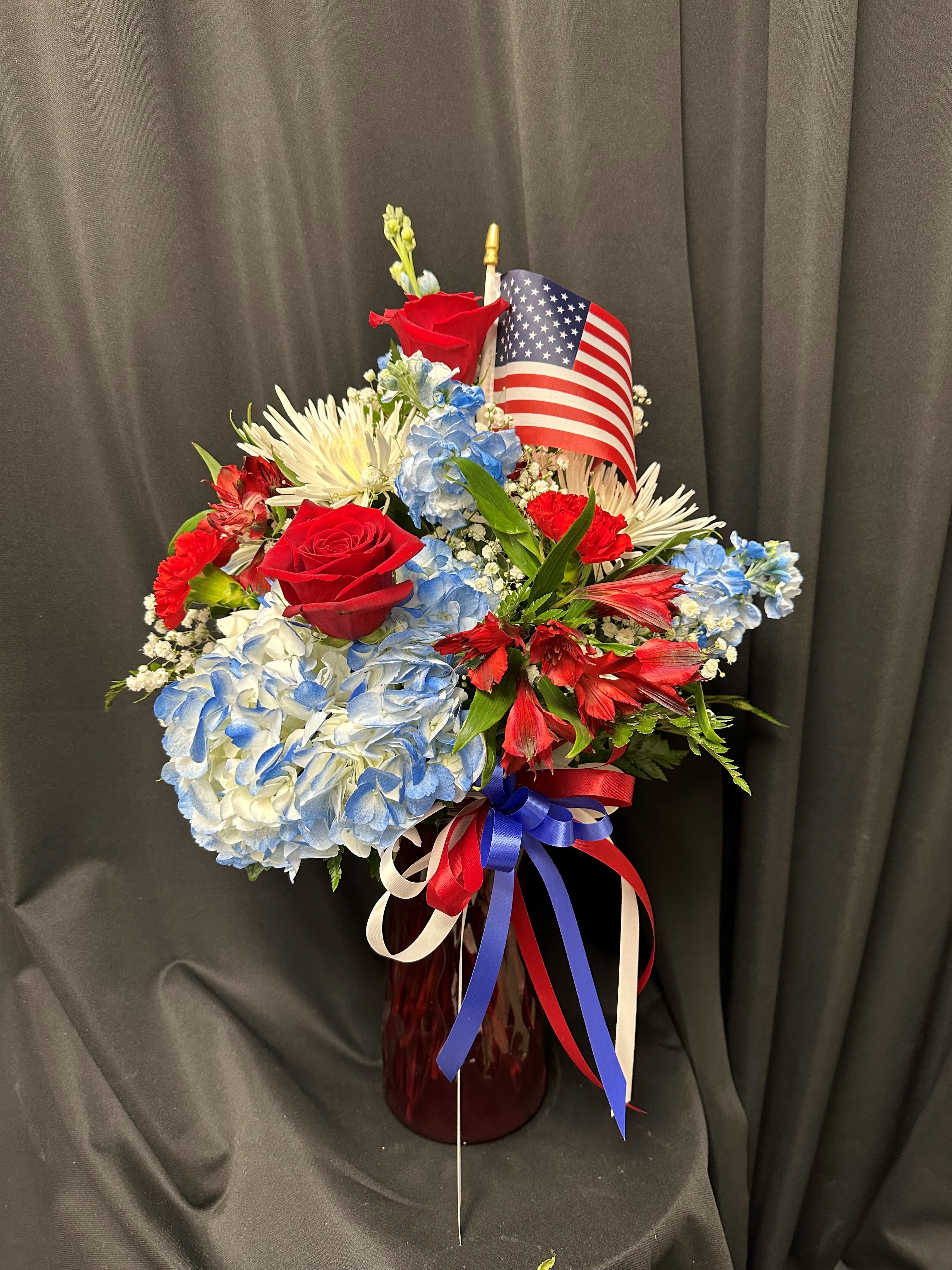 Red, white, and blue floral arrangement in a vase with an American flag