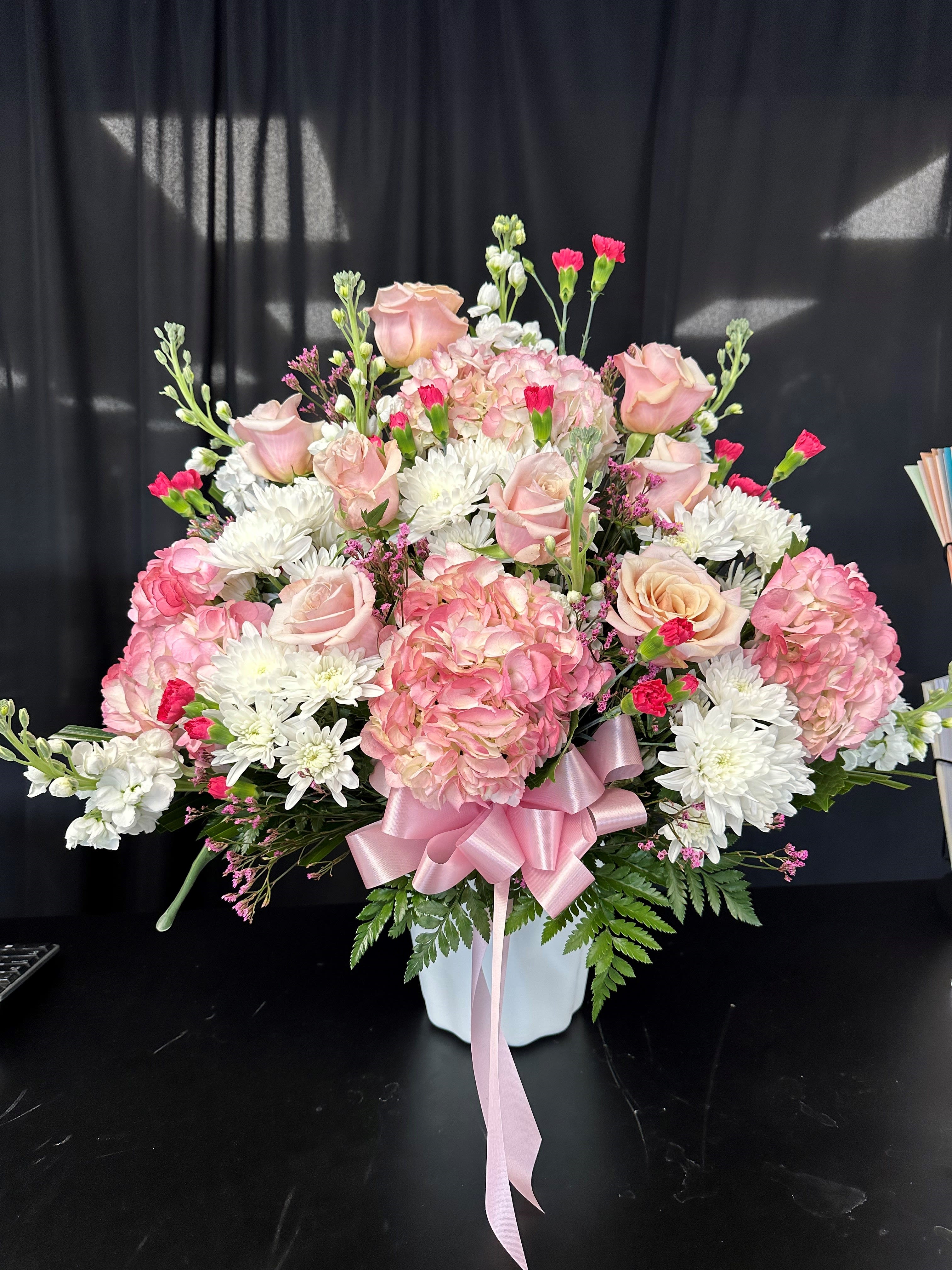 Pink roses and hydrangeas in a white vase with a pink ribbon