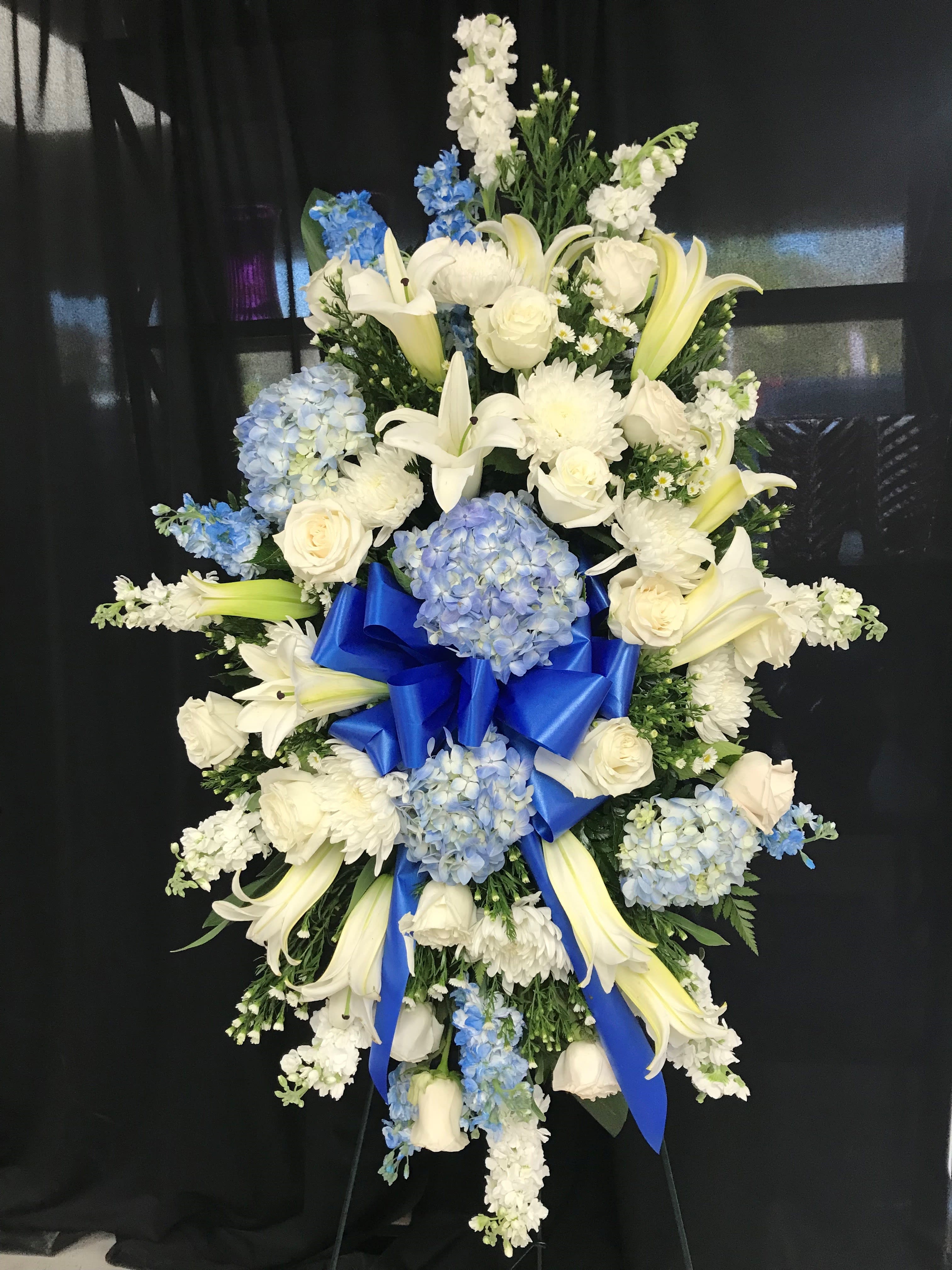 Standing floral spray with white lilies, roses, and blue hydrangeas on a black backdrop