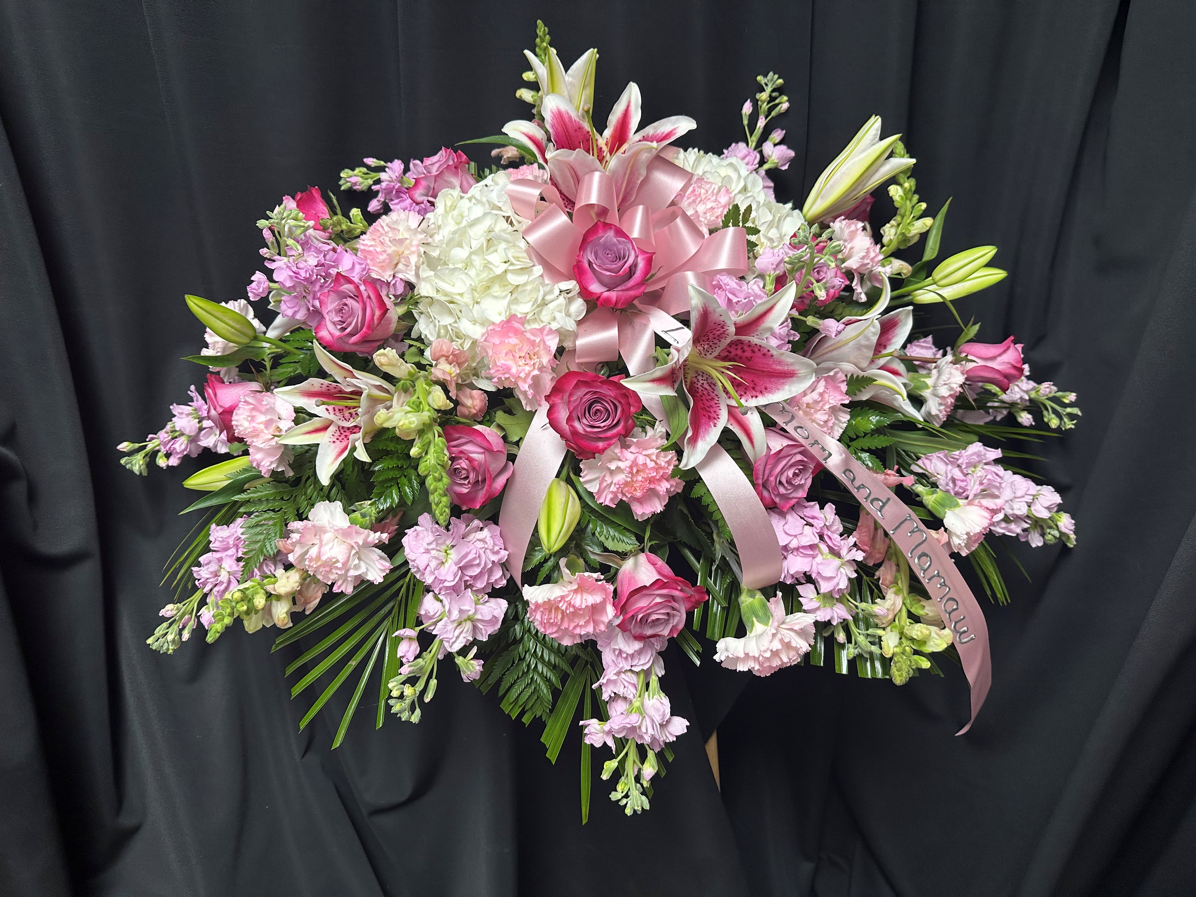 Pink and white floral spray with lilies, roses, and ribbon on a black backdrop