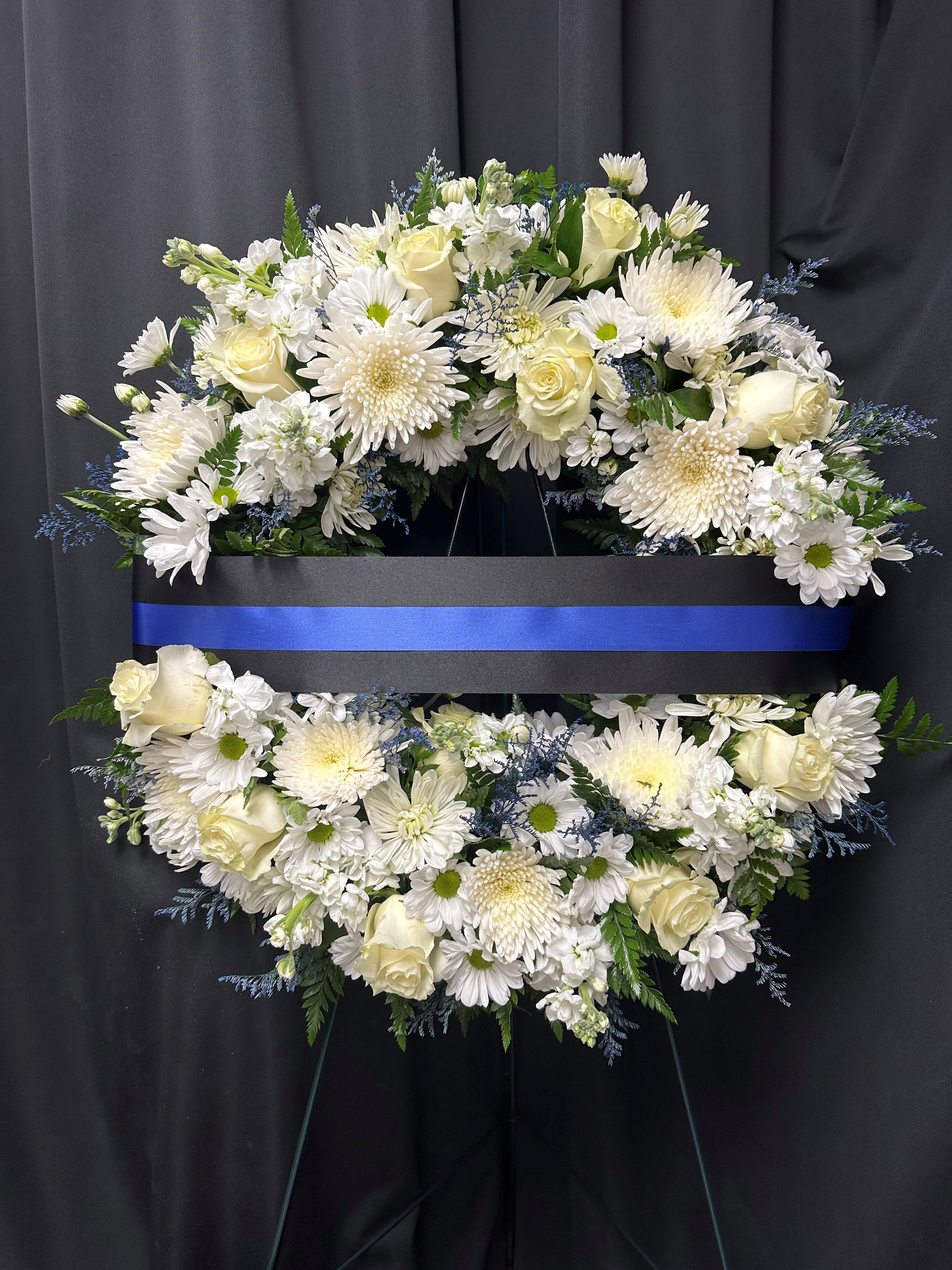 White floral funeral wreath with roses and daisies on a black stand