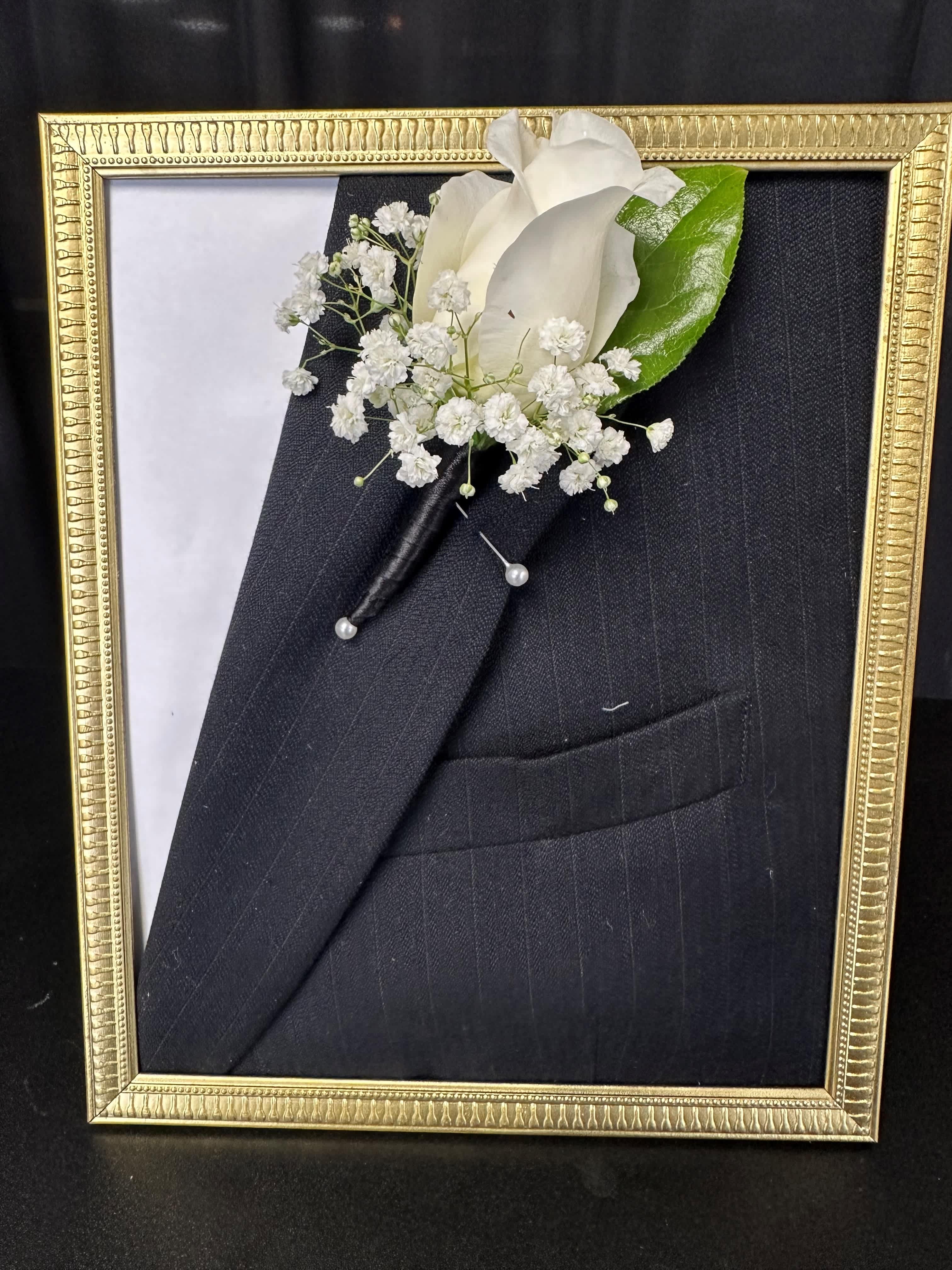 White boutonniere pinned to a black suit in a gold frame