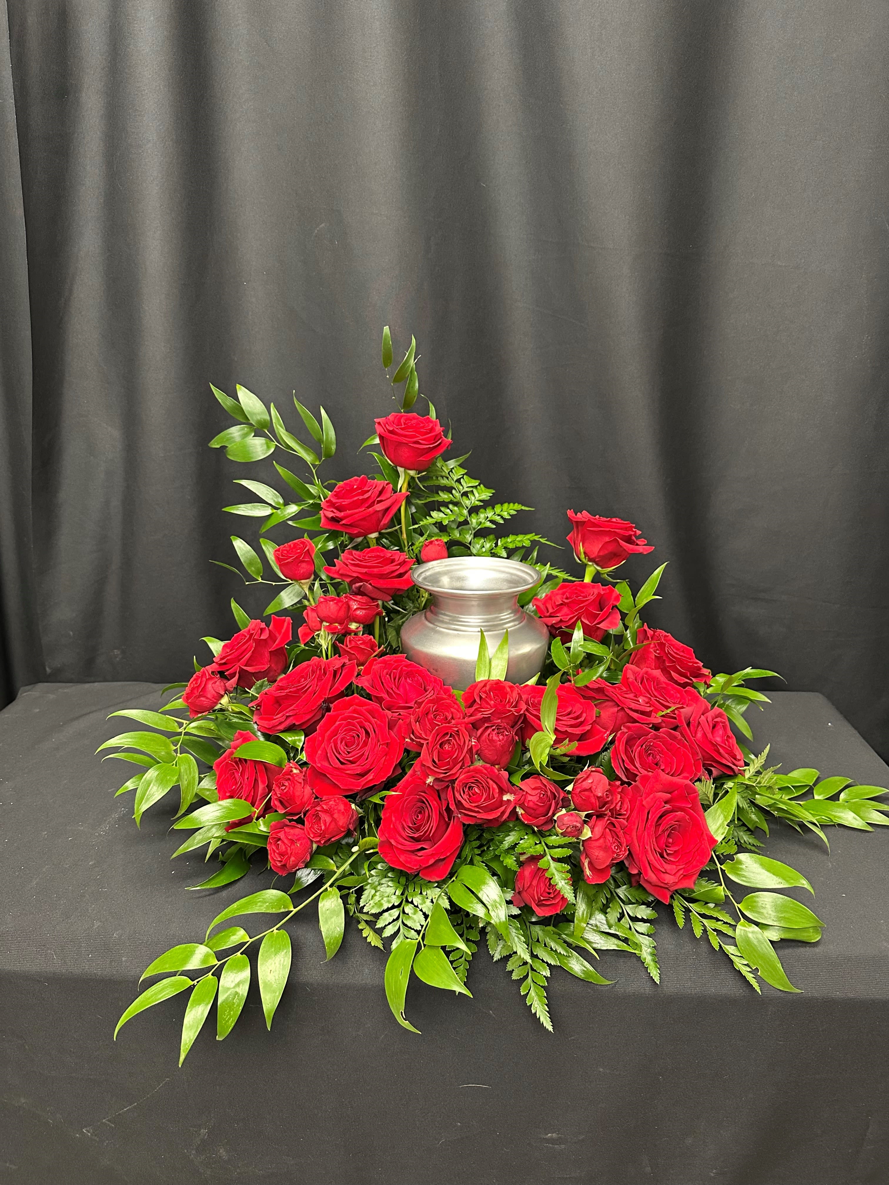 Red roses arranged around a silver urn on a black draped table