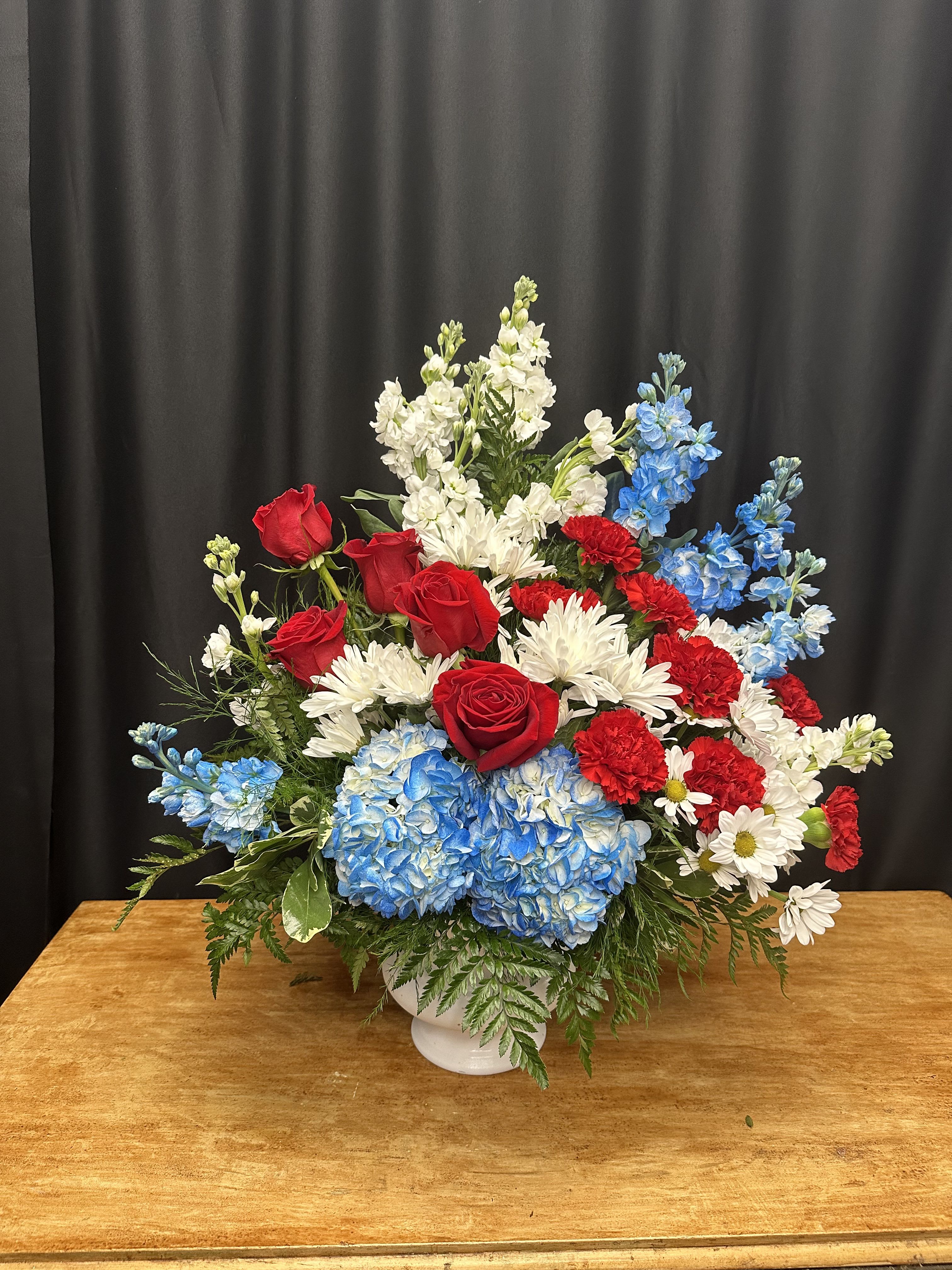 Red roses, blue hydrangeas, and white daisies in a white vase