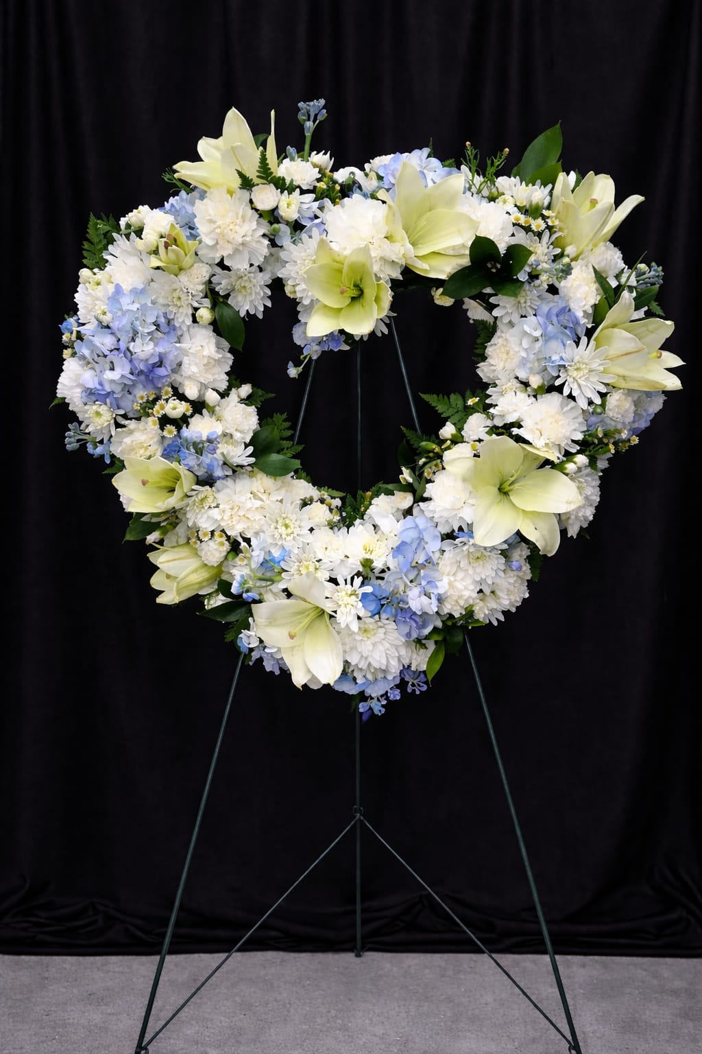 Heart-shaped floral wreath with white and pale blue flowers on a stand