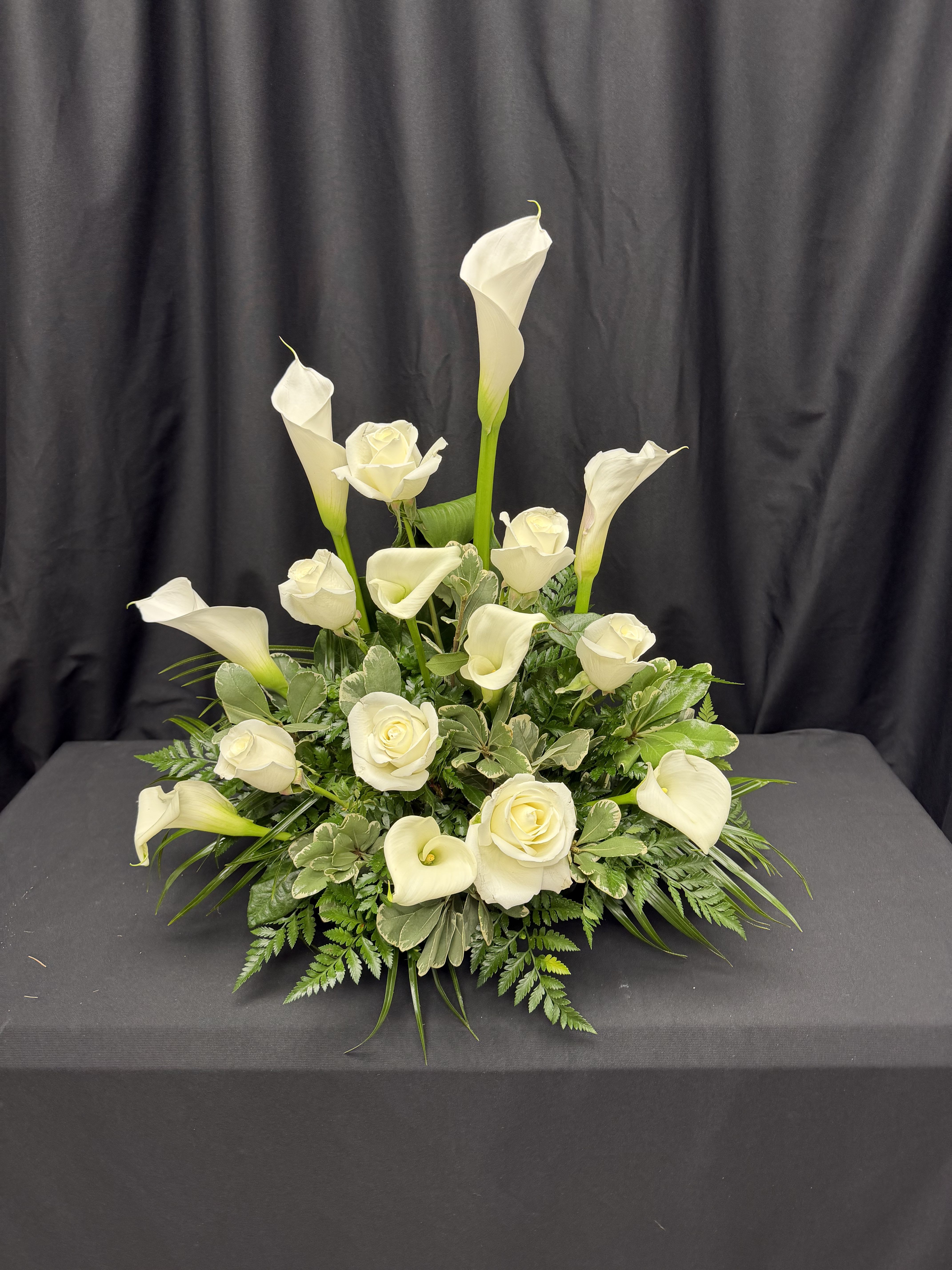 Calla Lily Comfort - The pristine beauty of white calla lilies and roses is showcased against a backdrop of lush greenery in this exquisite arrangement. Each bloom exudes elegance and purity, while the verdant foliage adds a touch of freshness and vibrancy. Whether adorning a special occasion or serving as a heartfelt expression of sympathy, this arrangement captures the essence of grace and sophistication, leaving a lasting impression on all who behold it.