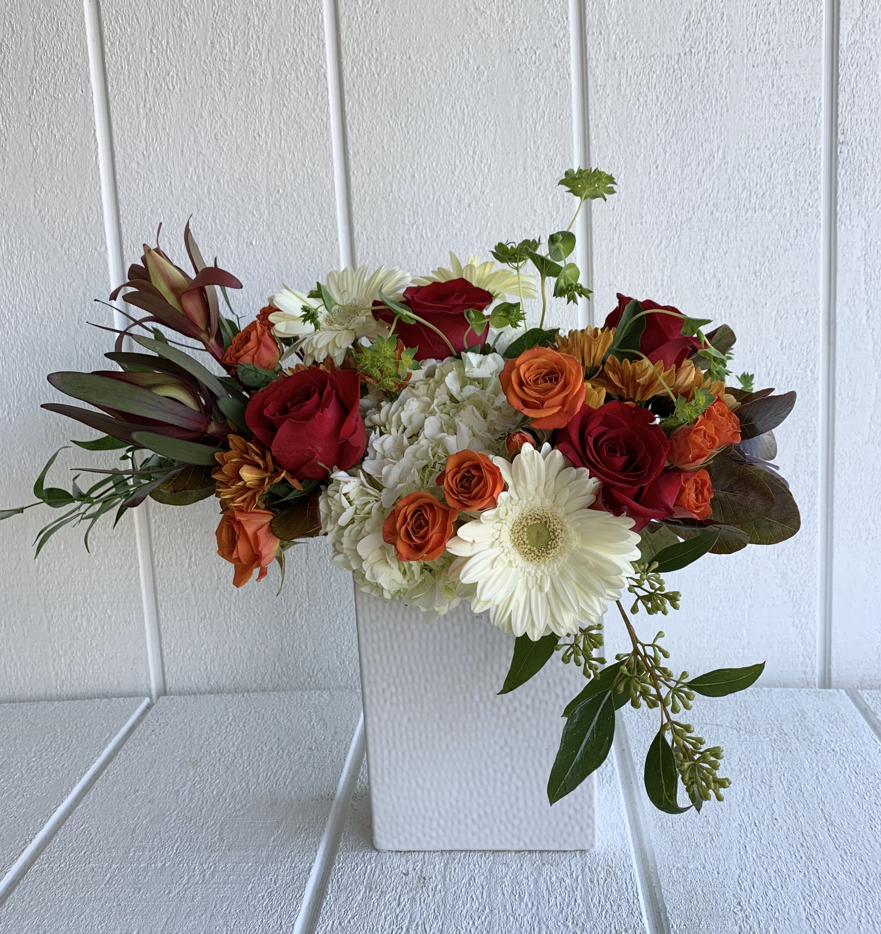 Mixed bouquet of red and orange roses with white daisies in a white vase