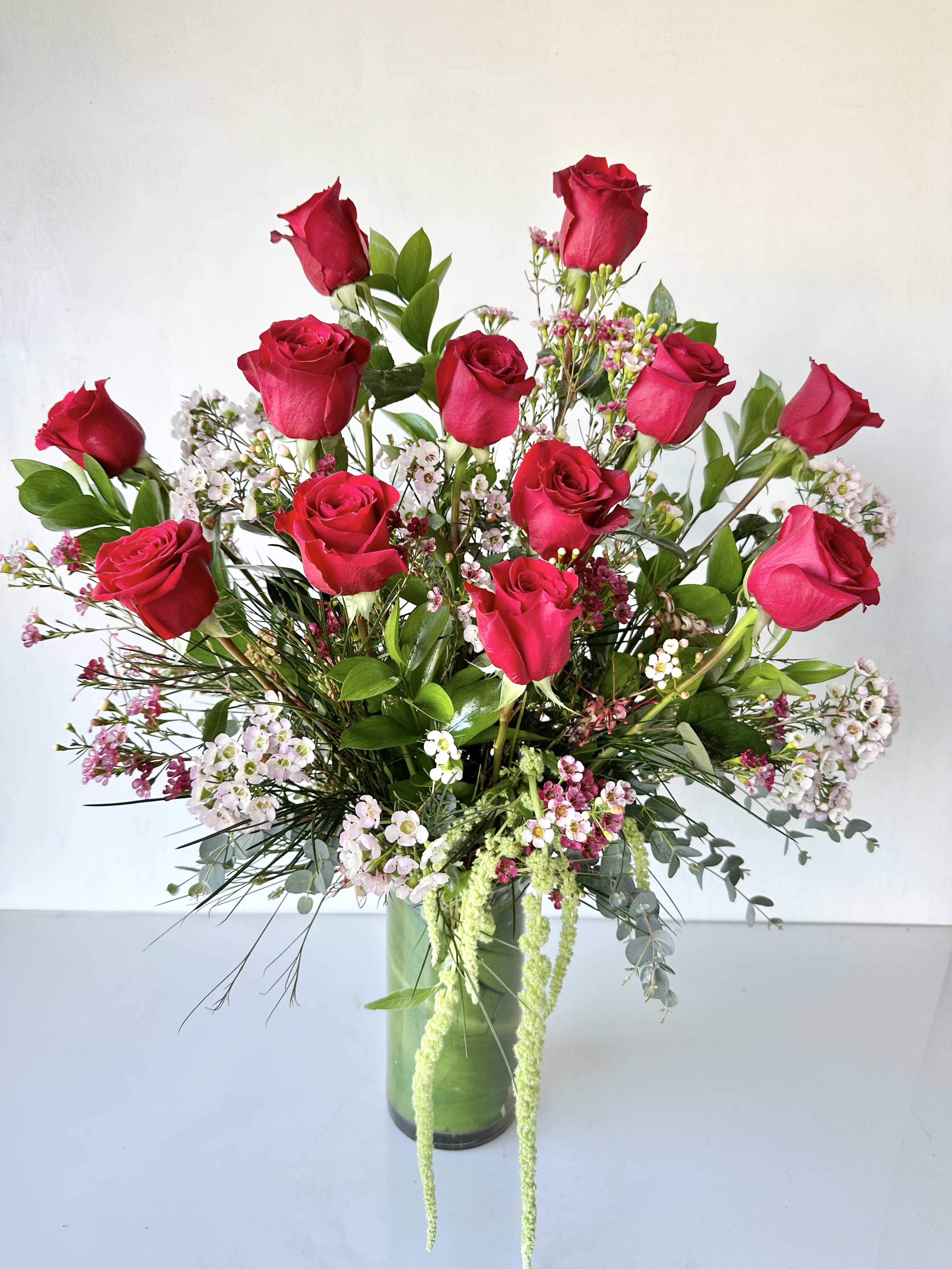 Tall bouquet of red roses and small pink-white filler flowers in a glass vase