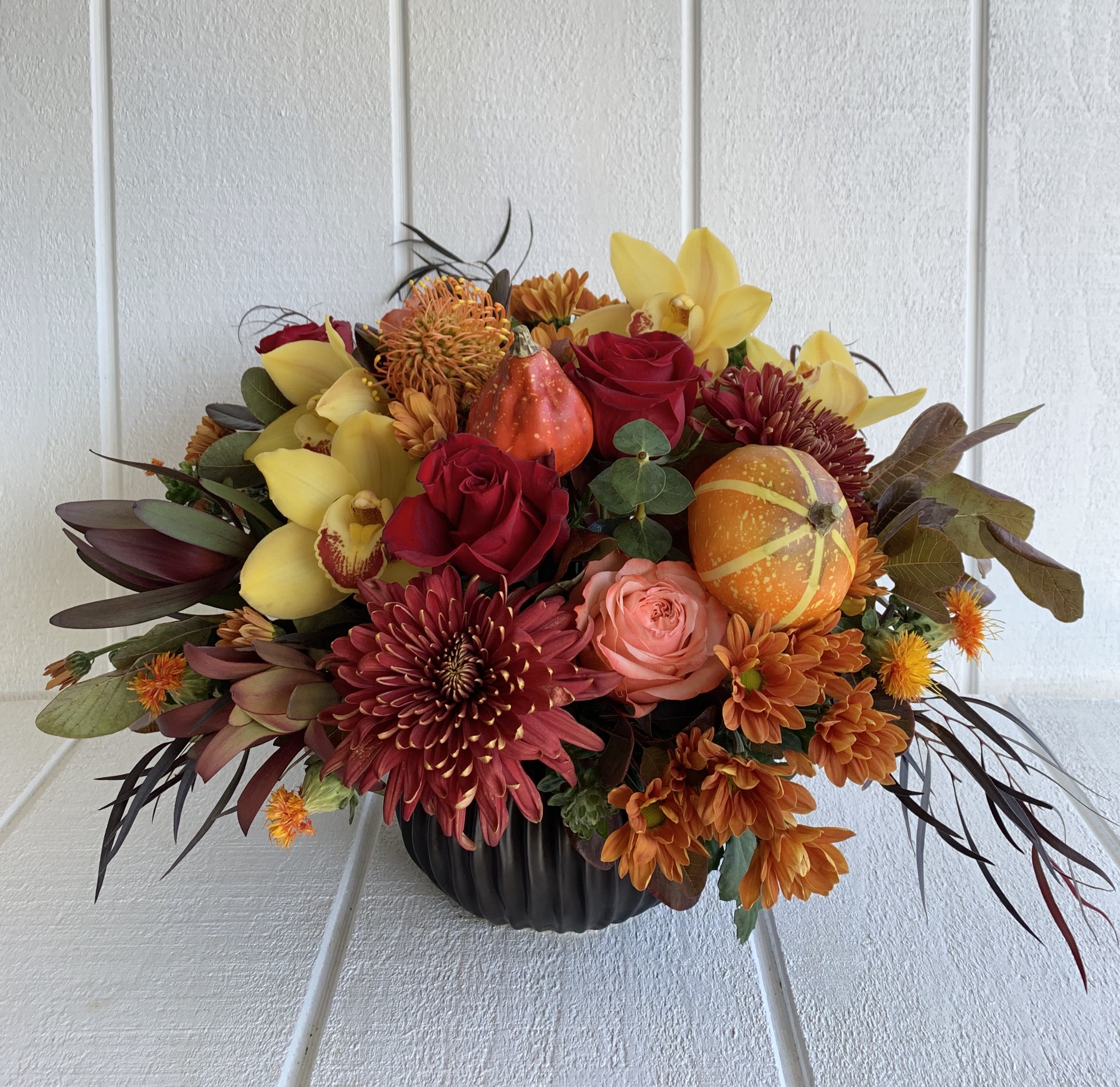 Autumn floral arrangement in a black pumpkin vase with roses and mums
