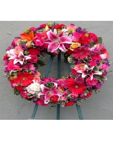 Circular floral wreath with pink, red, and white blooms on a stand