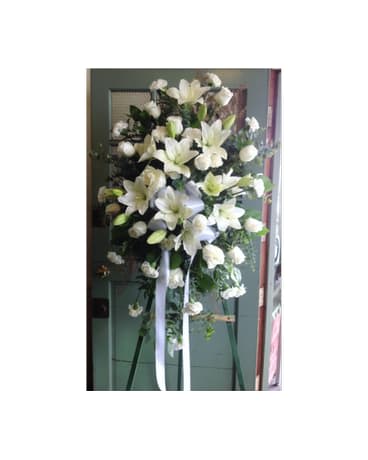 Tall white lily standing spray on an easel with ribbon streamers