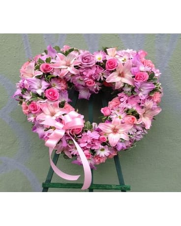 Heart-shaped pink floral wreath on a stand with ribbon