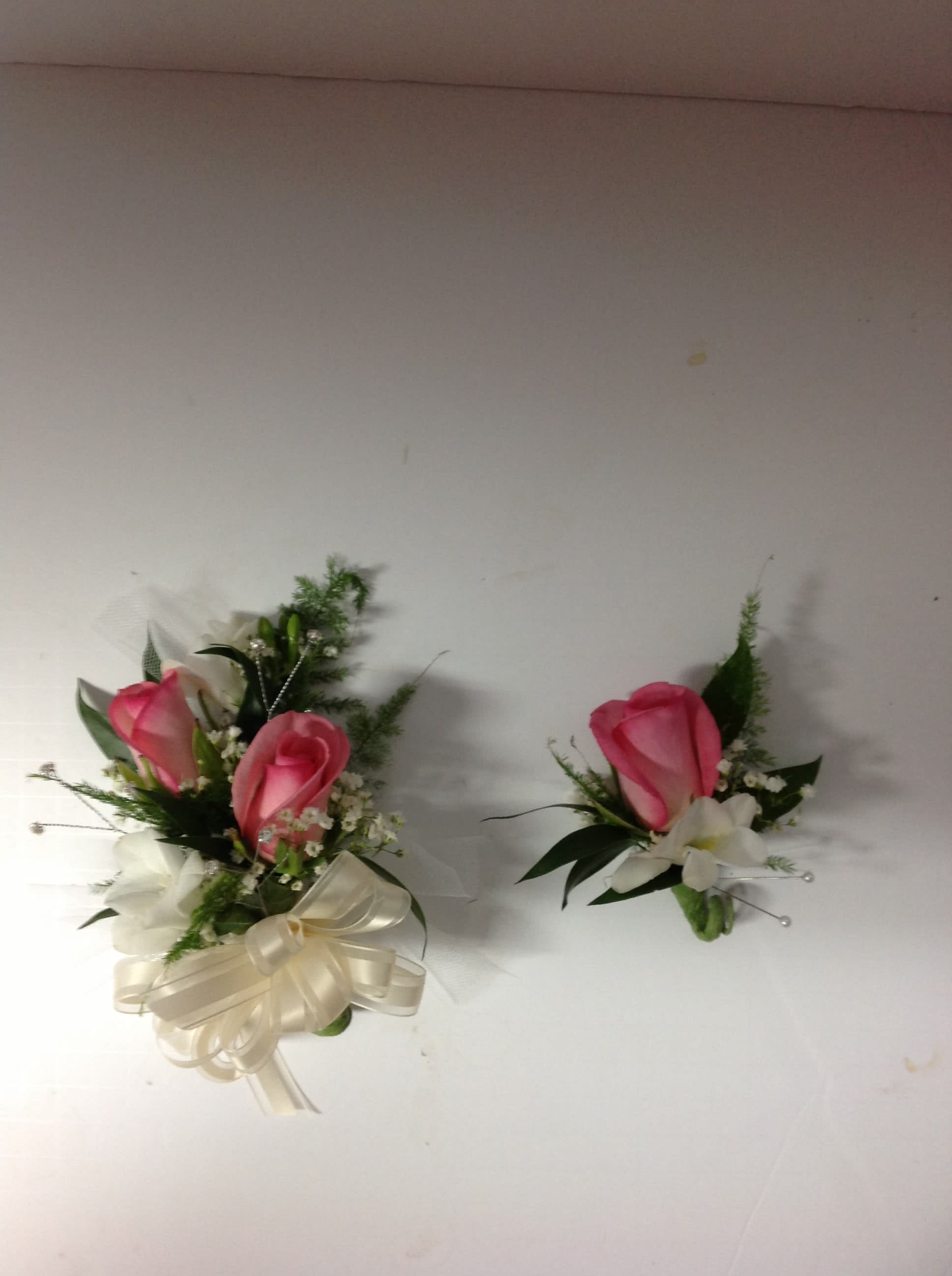 Two pink rose boutonnieres with white flowers and ribbon accents