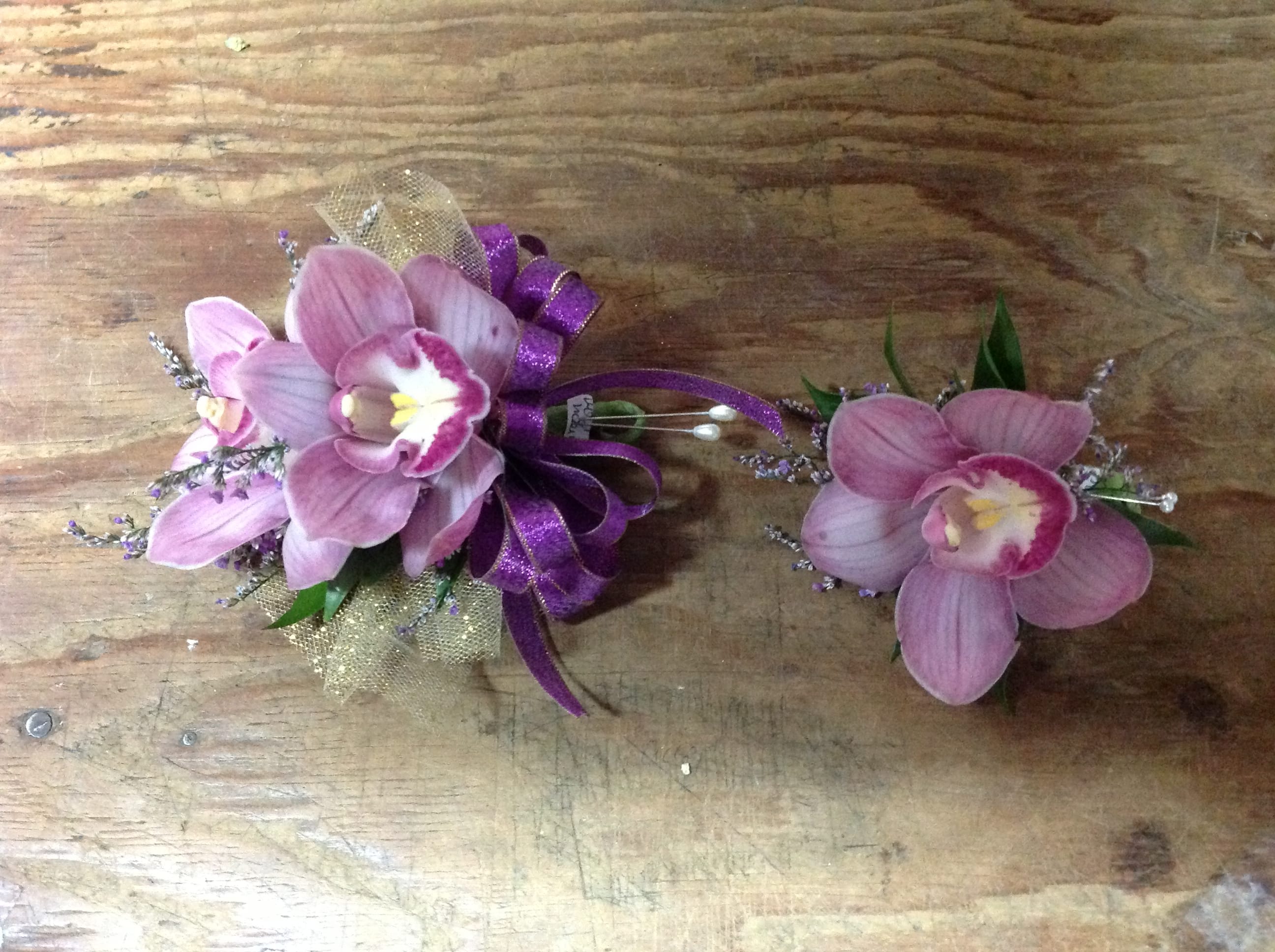 Two pink orchid corsages with purple ribbon on a wooden surface