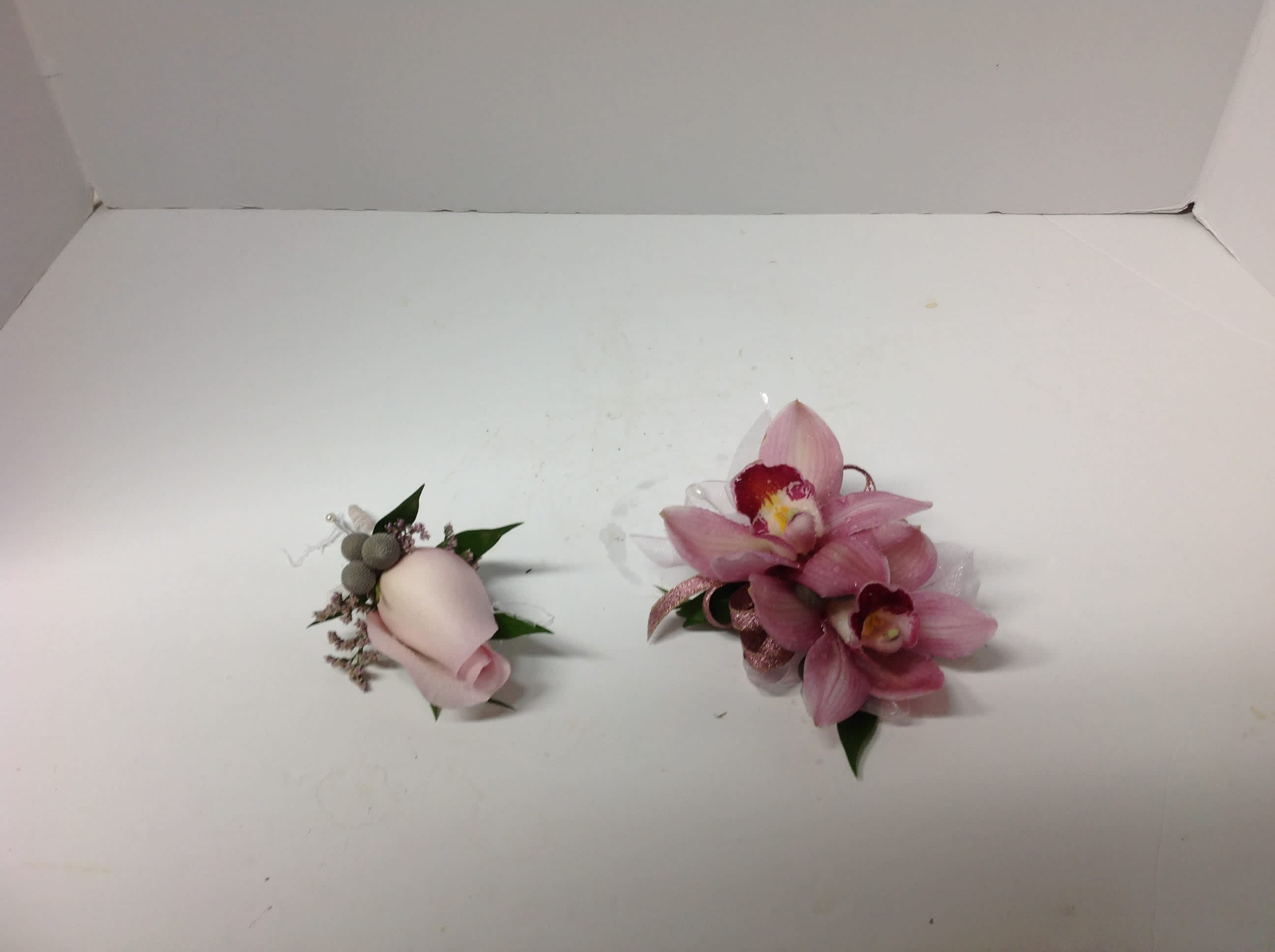 Two small pink floral corsages on a white surface