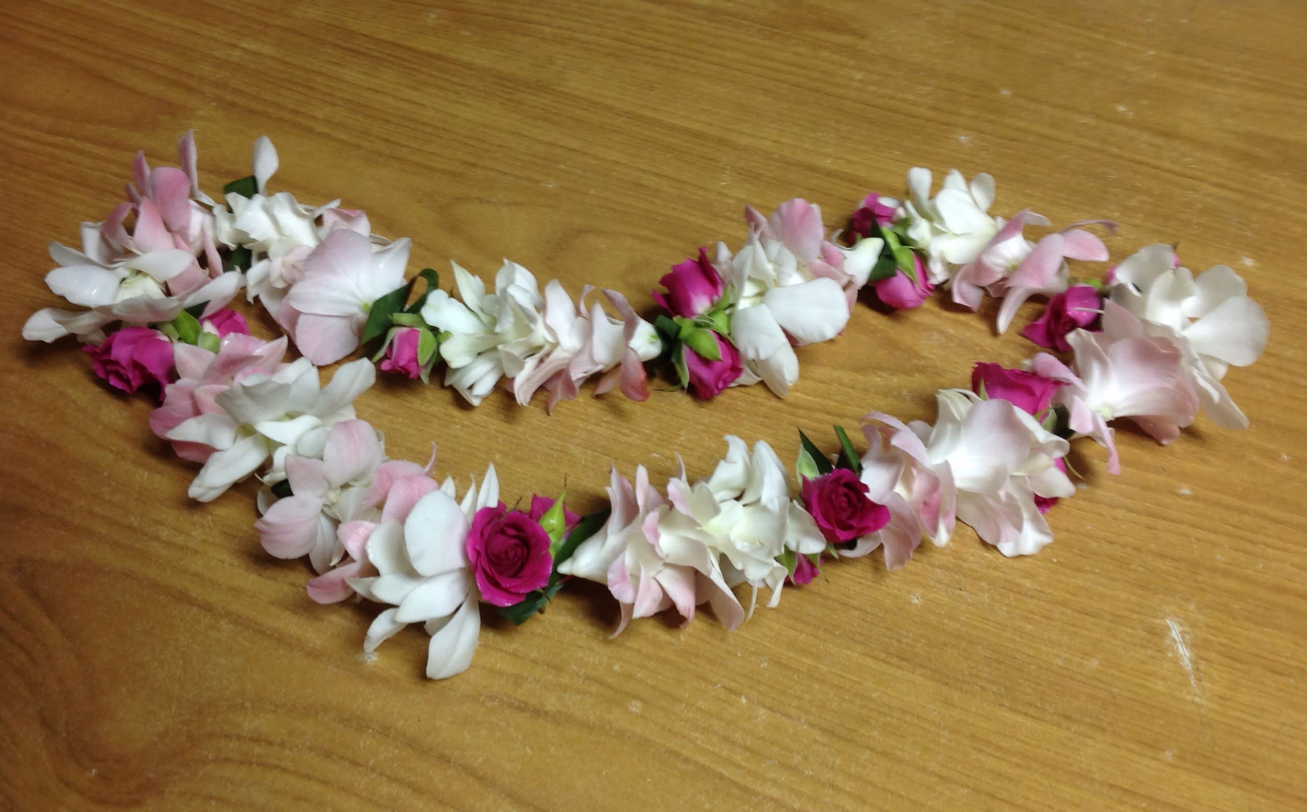Two floral garlands of pink and white blossoms on a wooden surface