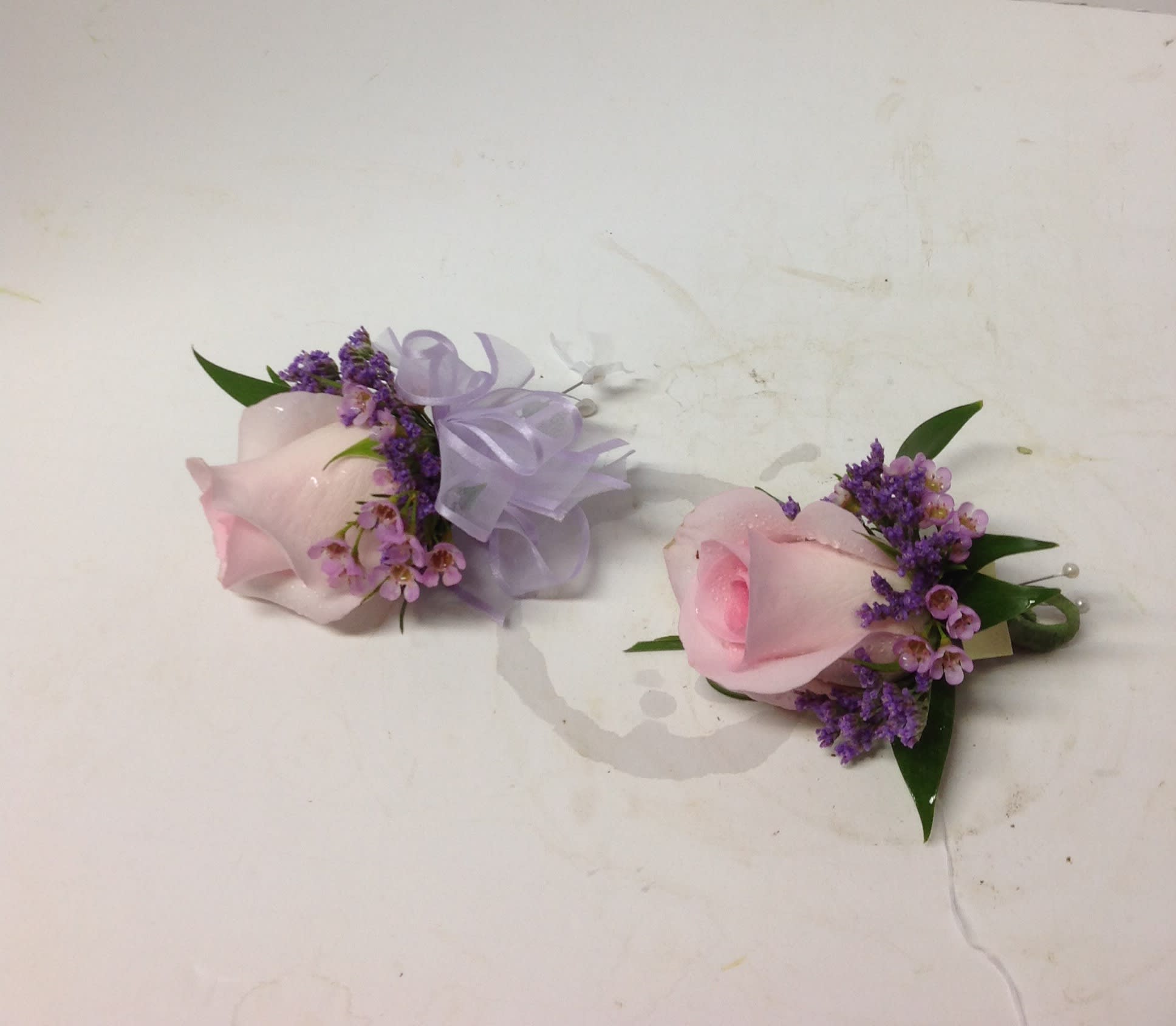 Two pink rose boutonnieres with purple filler and ribbon bows