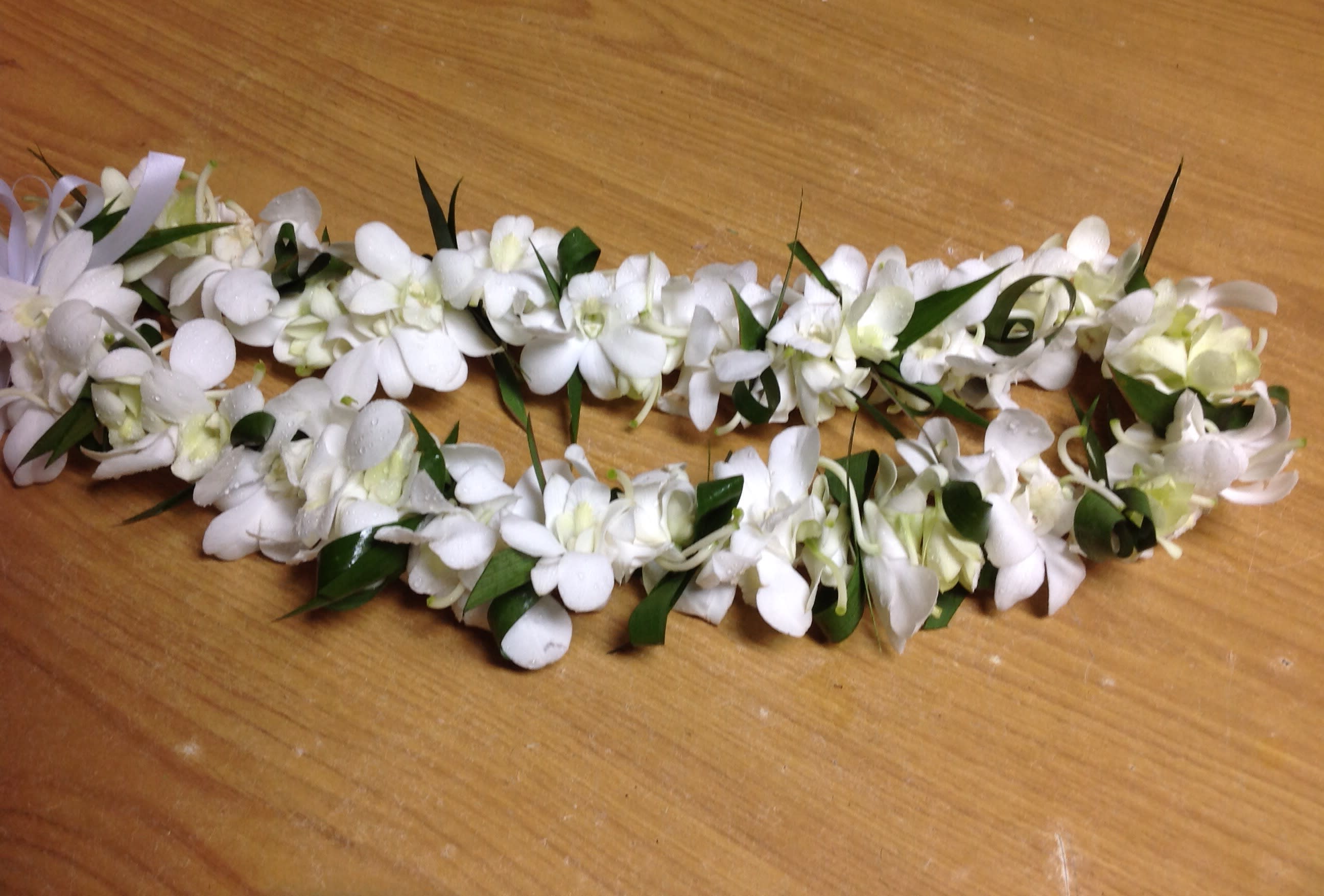 White floral lei with green leaves on a wooden surface