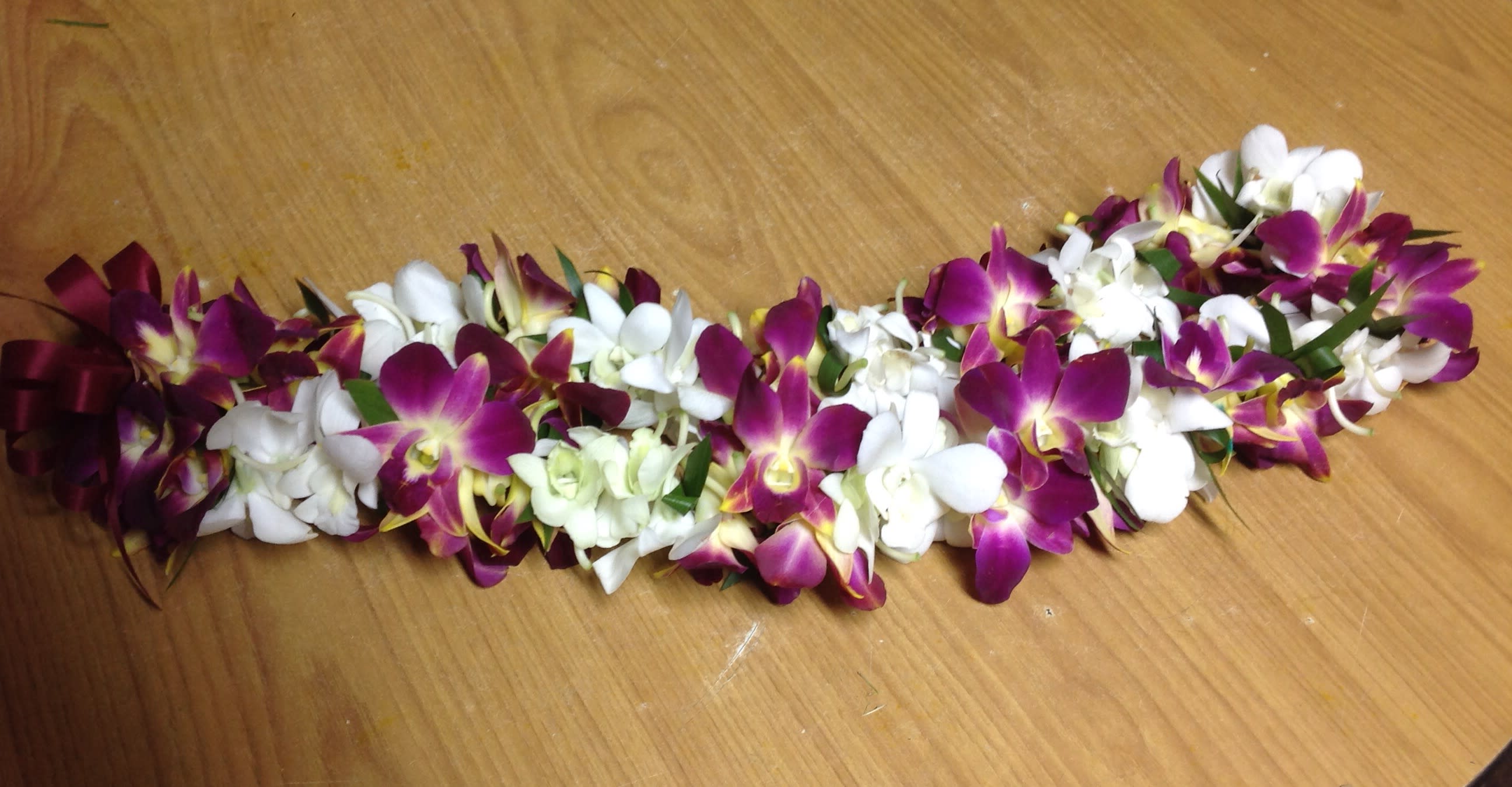Purple and white orchid lei laid on a wooden surface