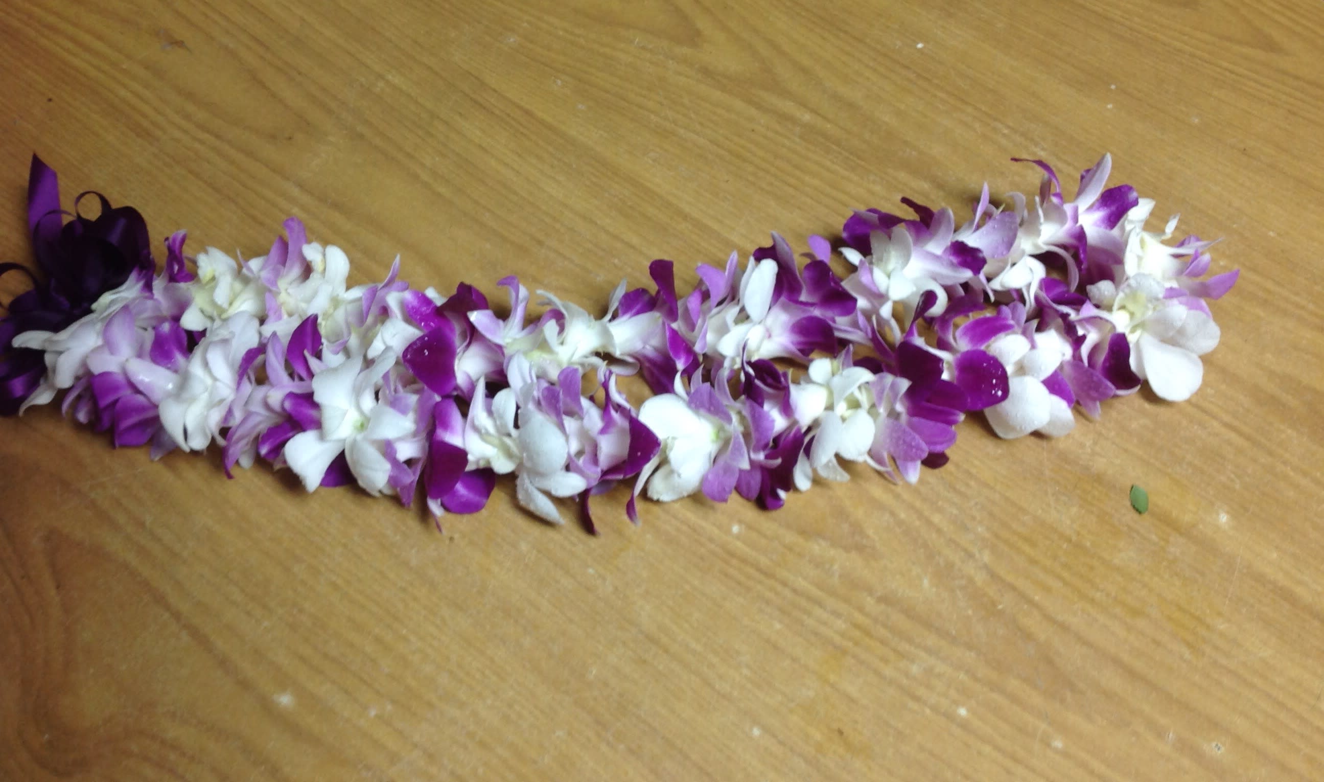 Purple and white orchid lei laid on a wooden surface