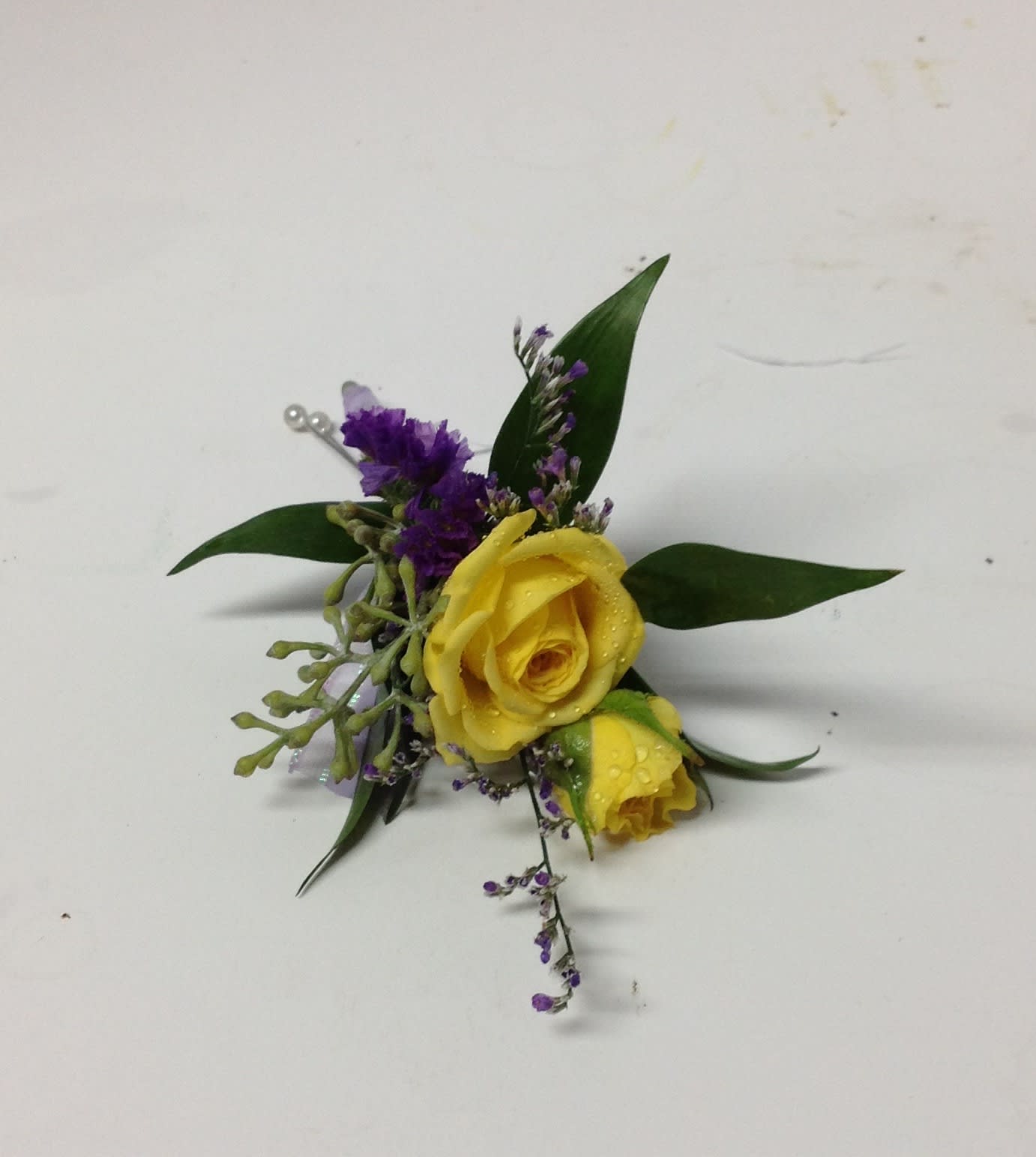 Yellow rose boutonniere with purple filler and green leaves