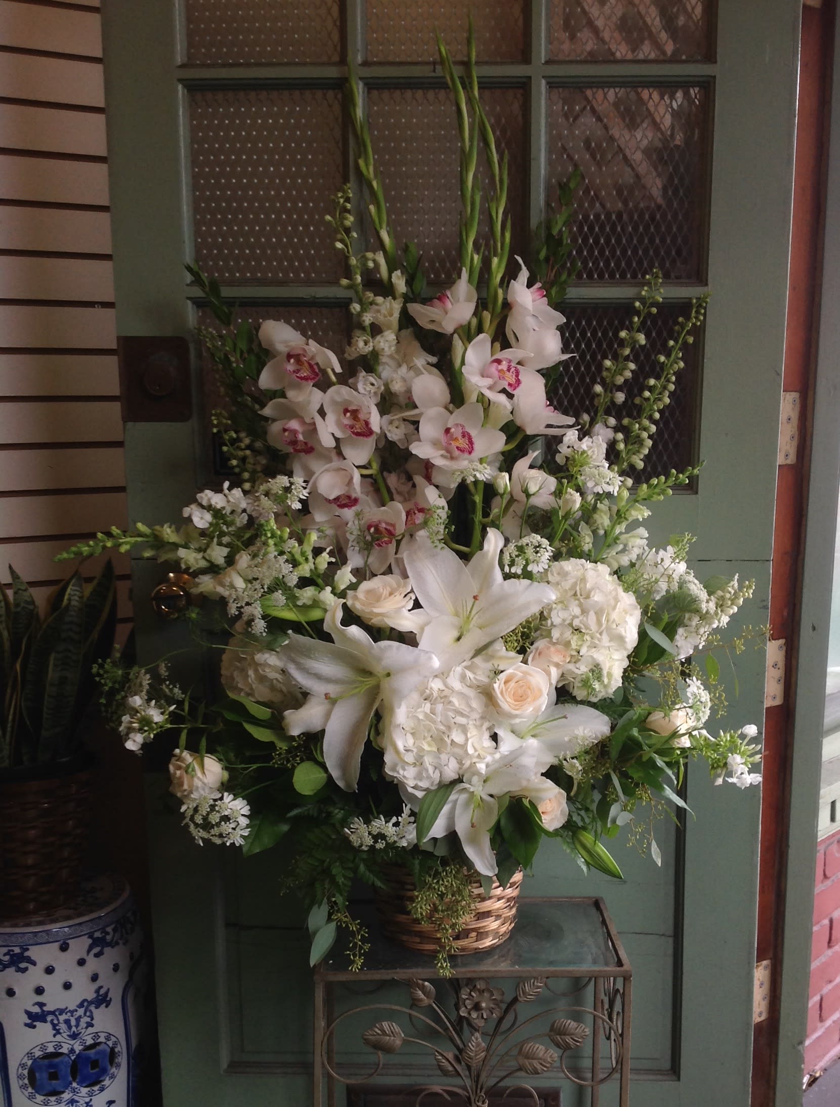 Tall white floral arrangement in a wicker basket with lilies and orchids