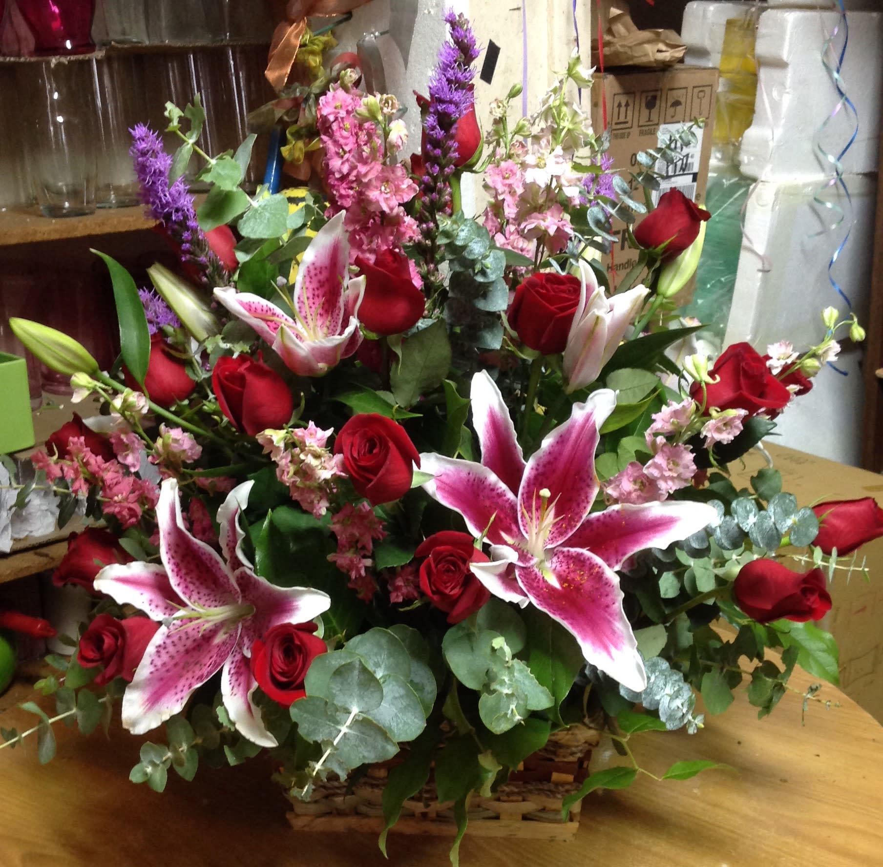Basket arrangement of red roses and pink lilies with purple accents