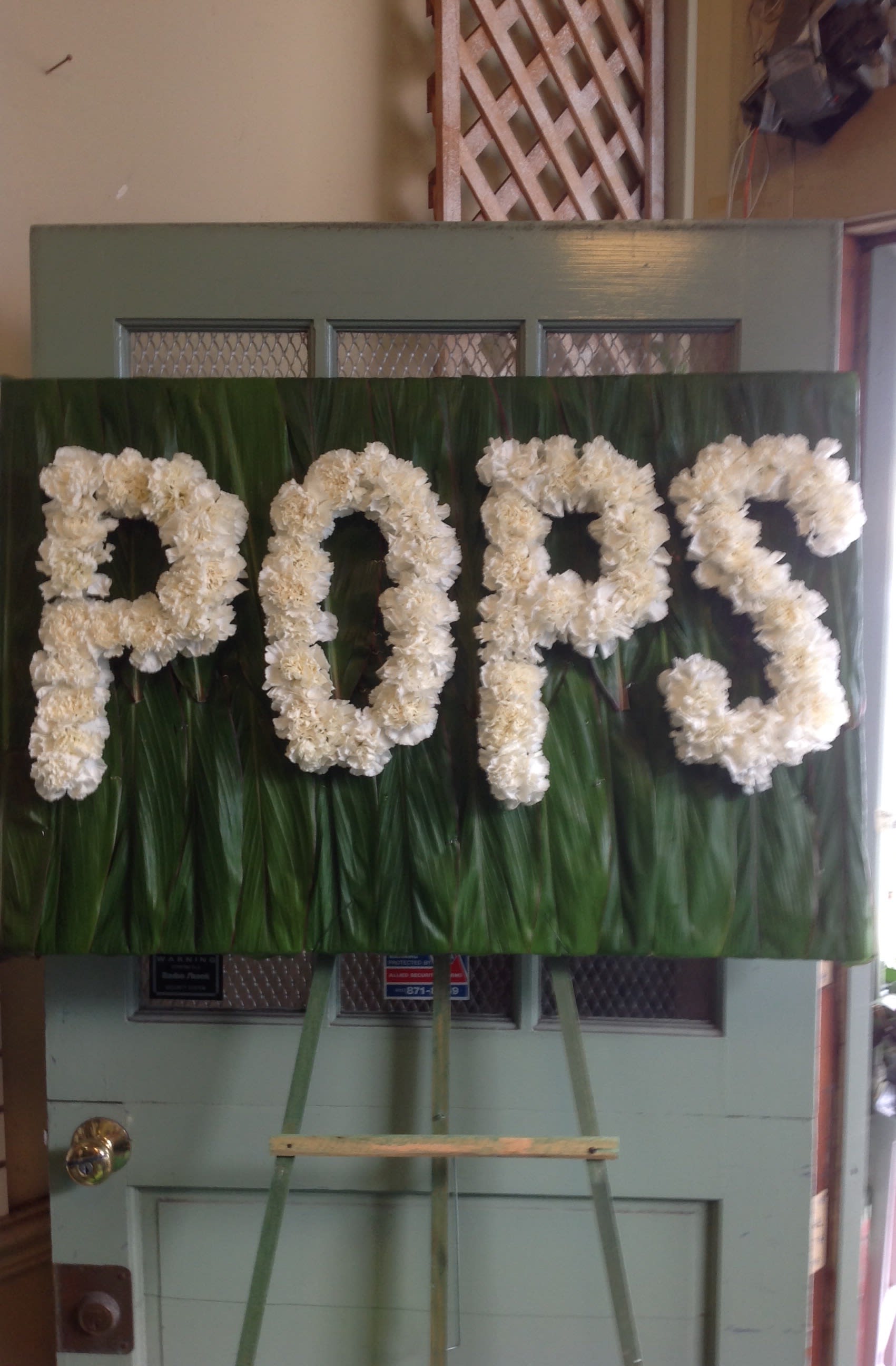 White floral letters spelling "POPS" on a green backdrop.