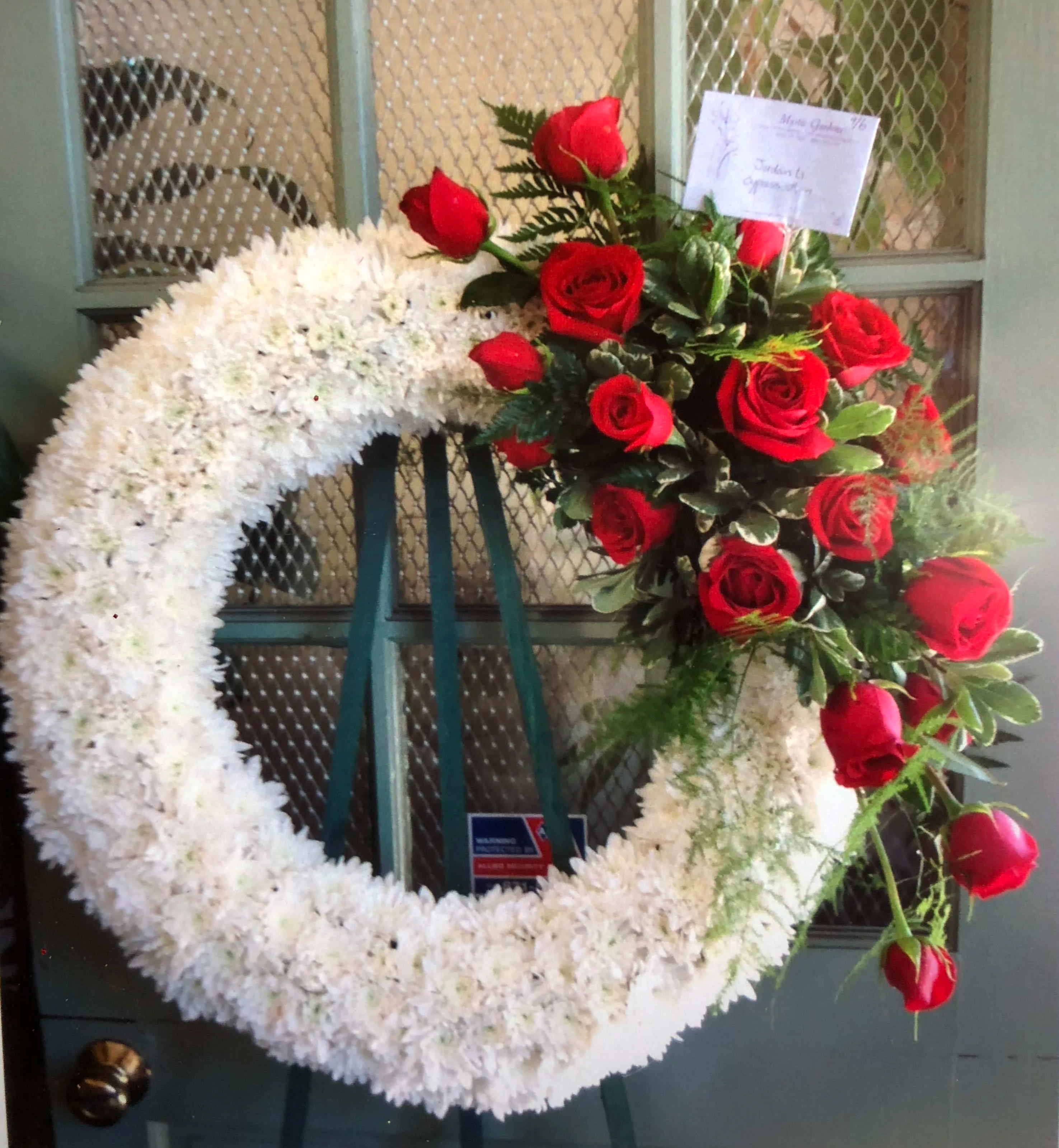 White floral wreath with red roses on a stand