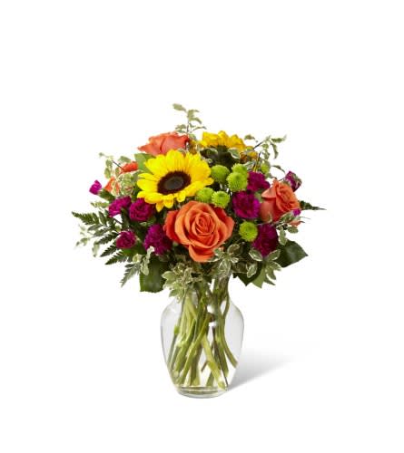 Mixed bouquet with sunflowers, orange roses, and magenta blooms in a glass vase