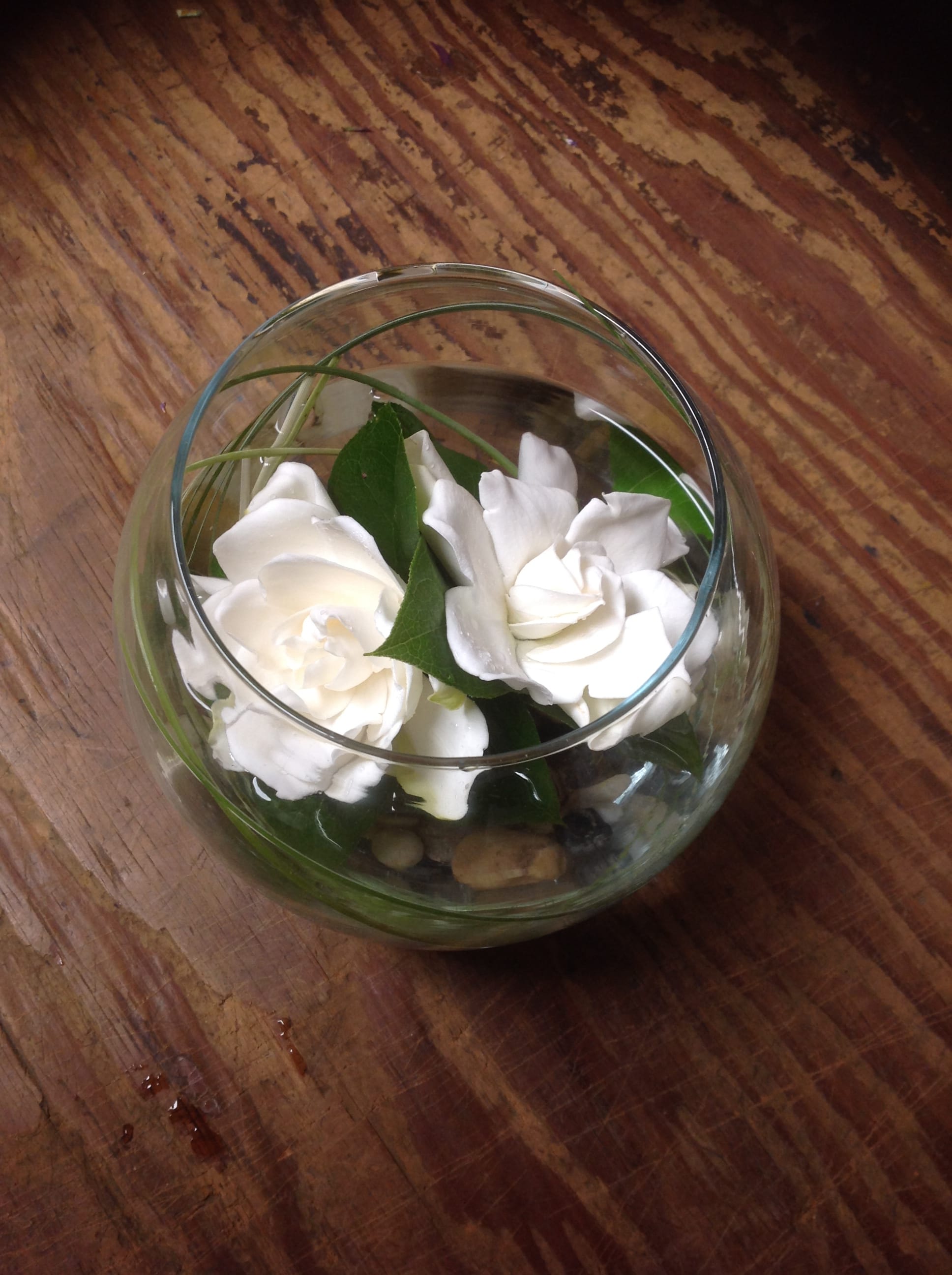 White flowers arranged in a round glass bowl with stones