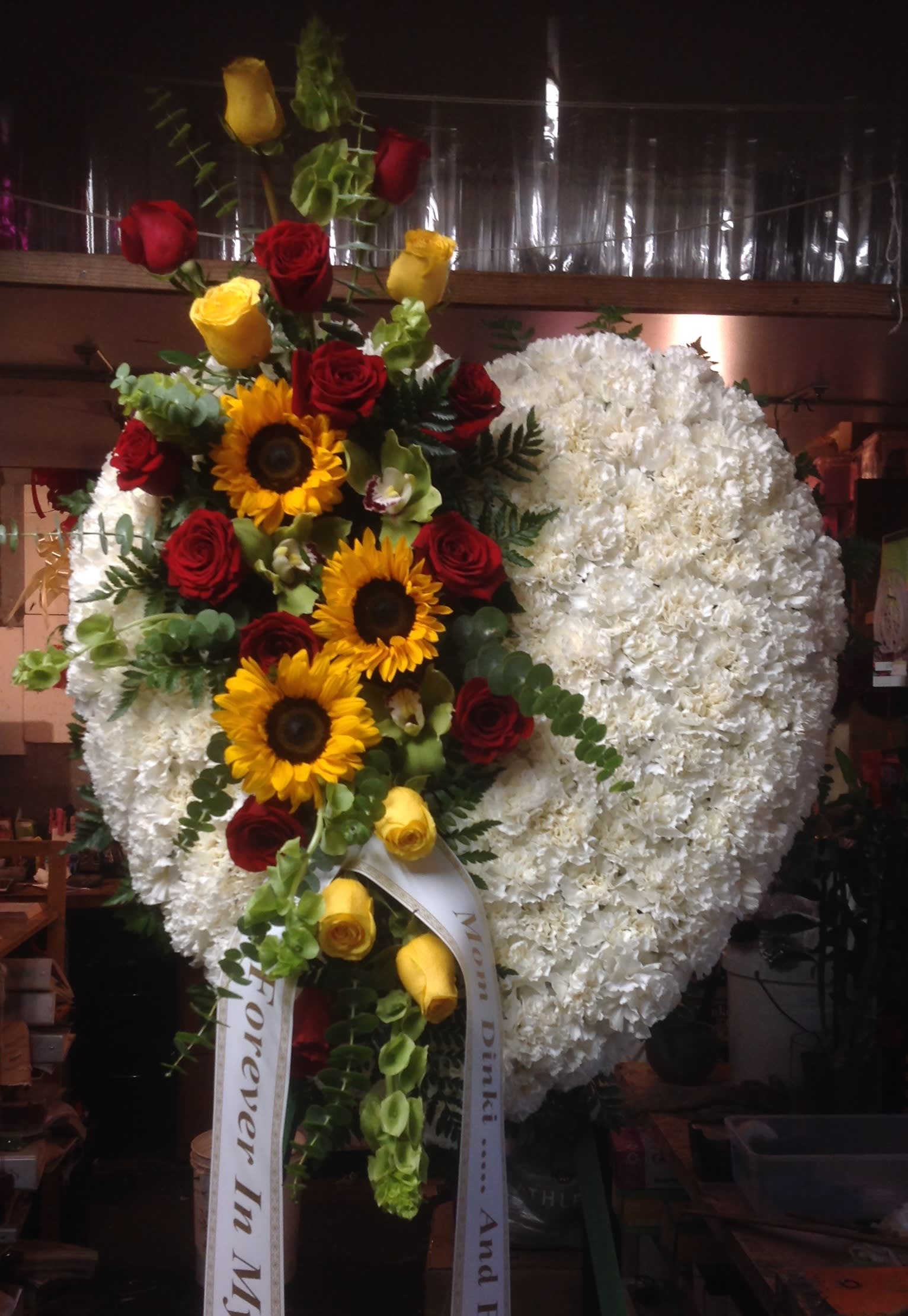 Large heart-shaped floral spray with white flowers, red and yellow roses, and sunflowers